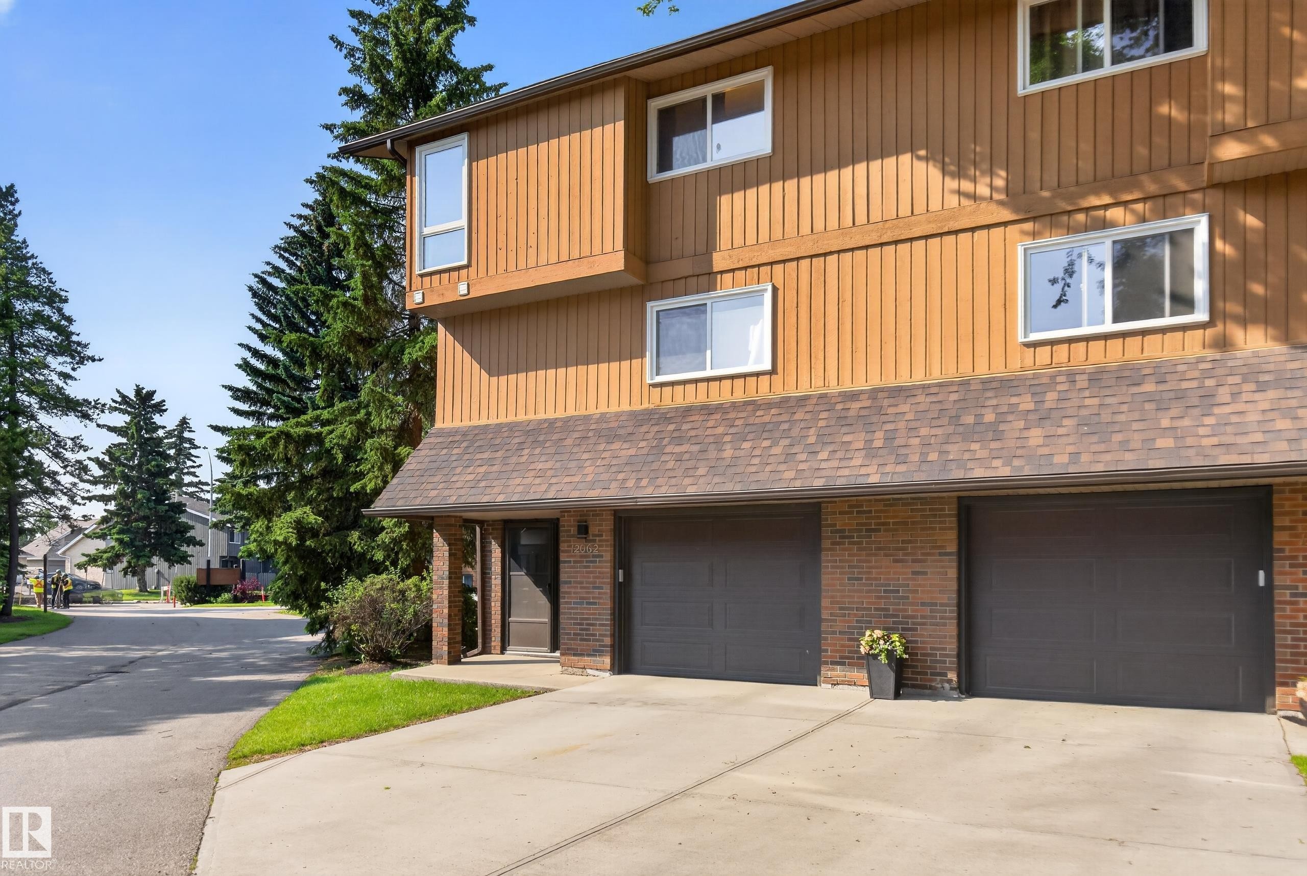 Two-story townhome featuring a brown vertical siding exterior and a multi-car driveway - 12062 157 Avenue, Edmonton, AB