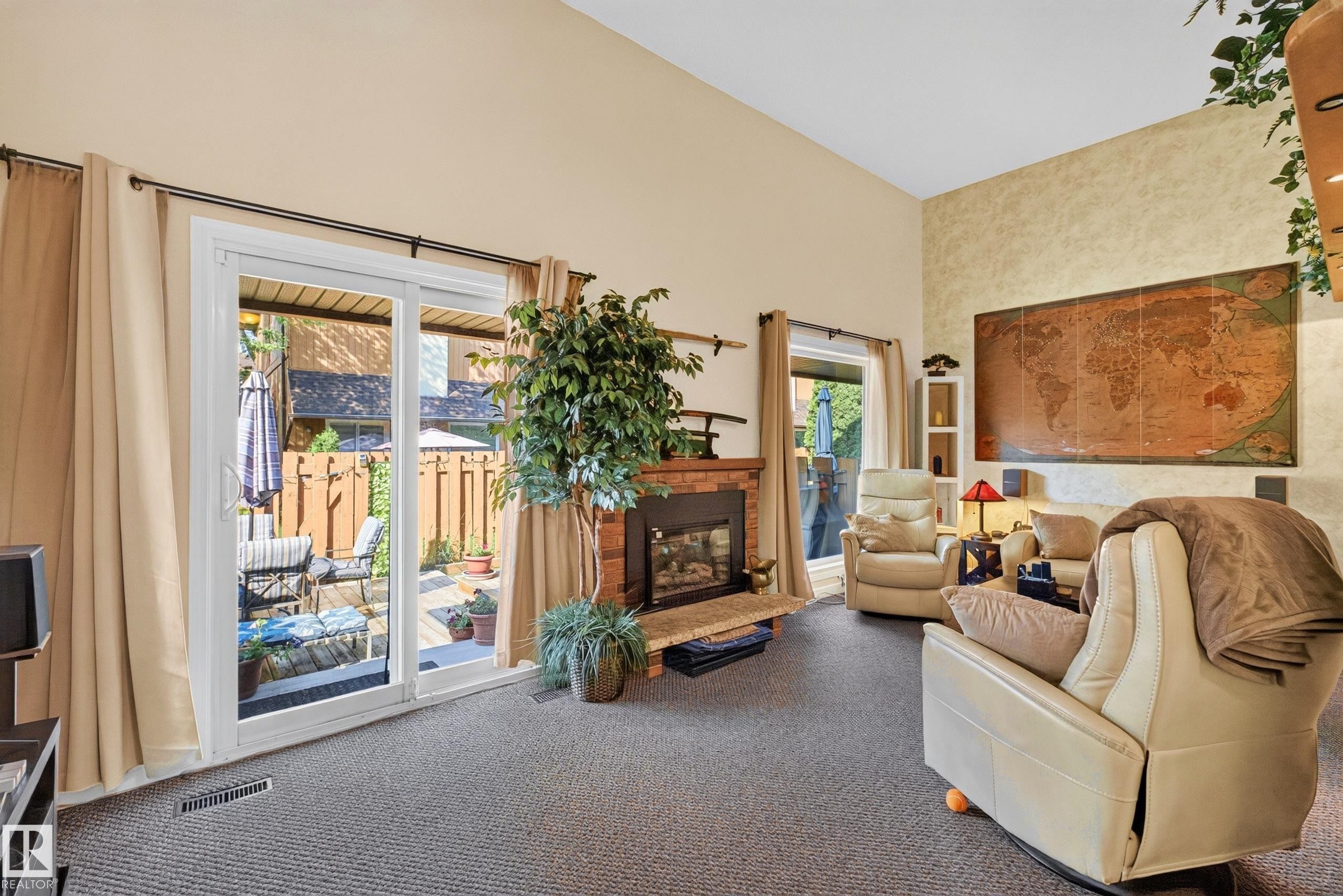 Spacious living area featuring a fireplace with a stone surround, a high vaulted ceiling, and sliding glass doors leading to an outdoor patio with privacy fencing - 12062 157 Avenue, Edmonton, AB