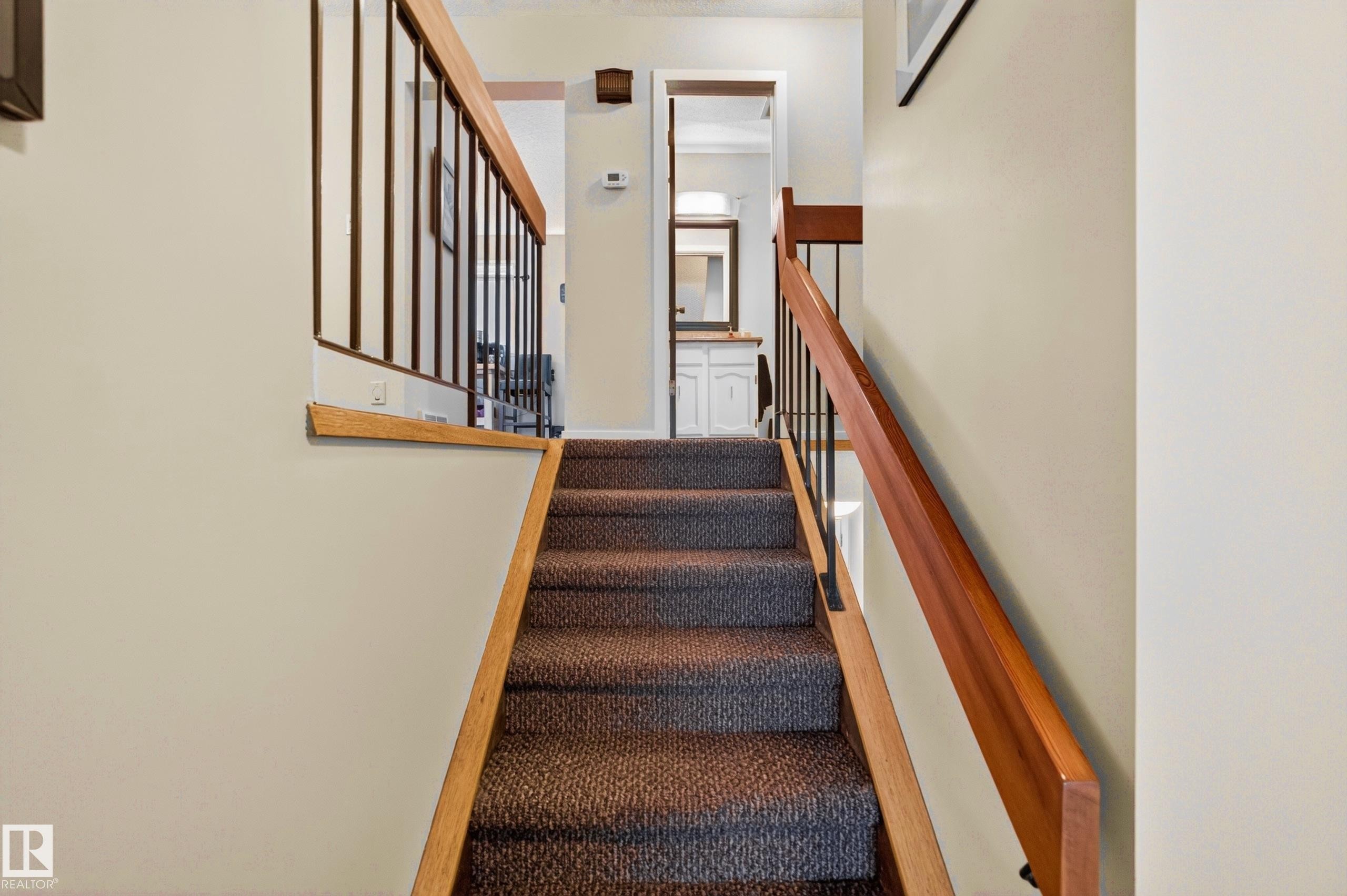 Carpeted staircase featuring wood handrails and black metal balusters - 12062 157 Avenue, Edmonton, AB