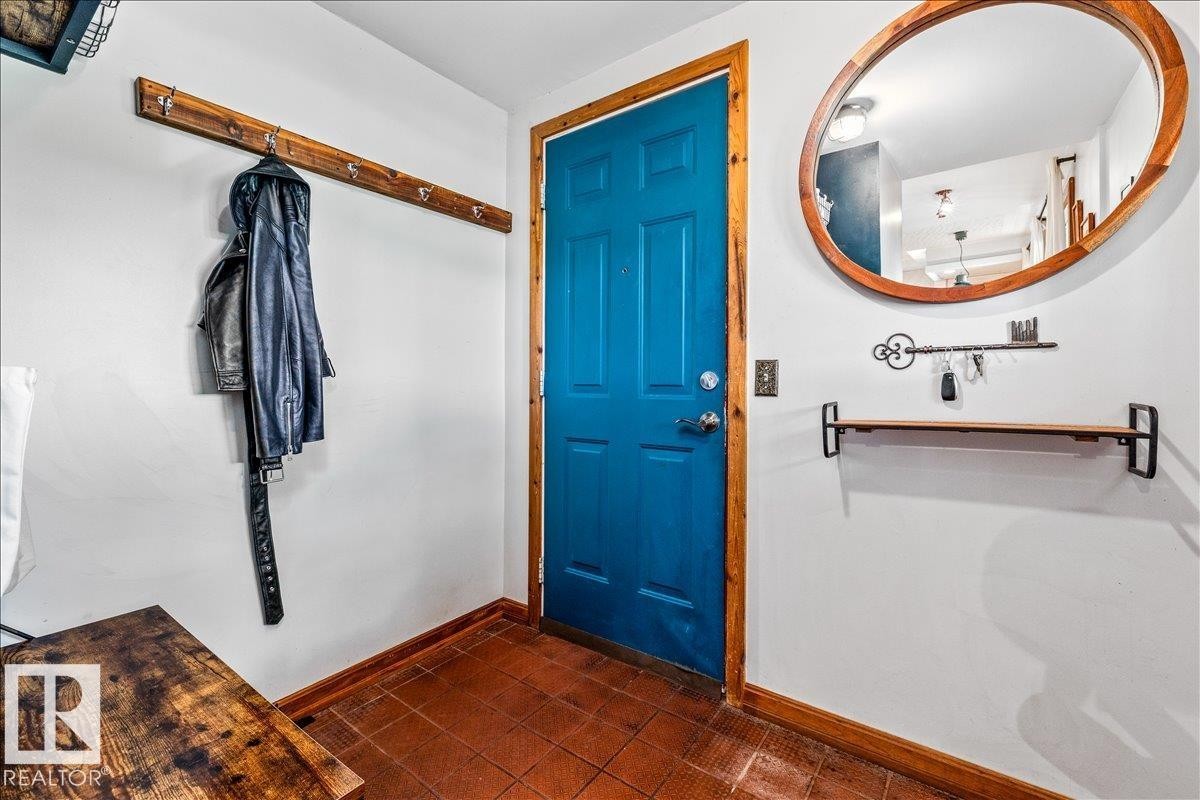 Entryway featuring a vibrant blue door with natural wood trim, terracotta floor tiling, and white wall finishes - 11603 70 Street Nw, Edmonton, AB