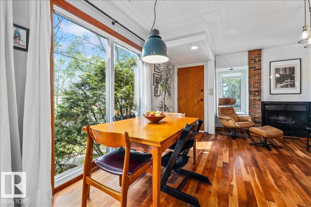 Bright interior space featuring expansive floor-to-ceiling windows, wood-finish flooring, a prominent brick fireplace, and a textured white ceiling - 11603 70 Street Nw, Edmonton, AB