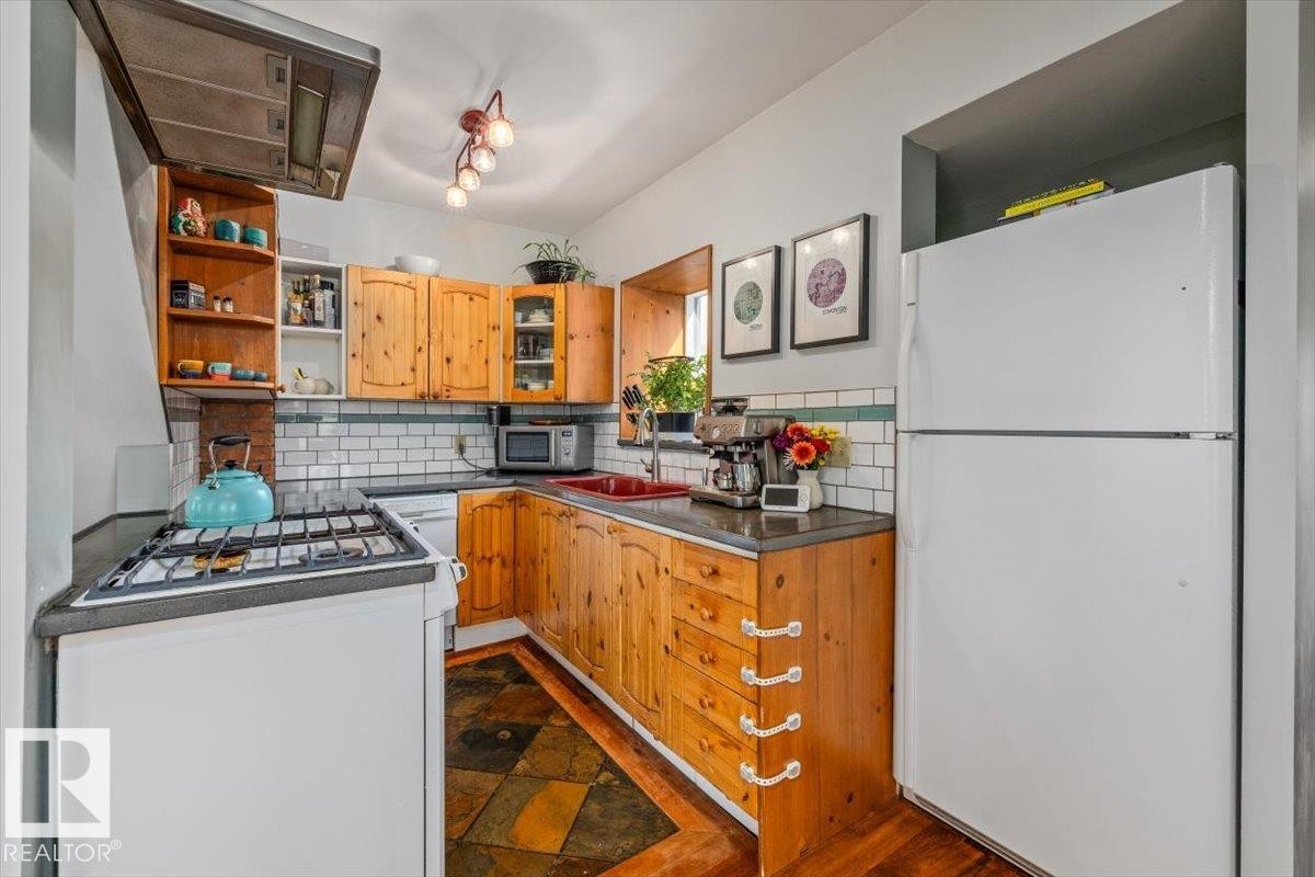 Kitchen featuring wood cabinetry, subway tile backsplash, slate-finish flooring, built-in range hood, and a red basin sink - 11603 70 Street Nw, Edmonton, AB