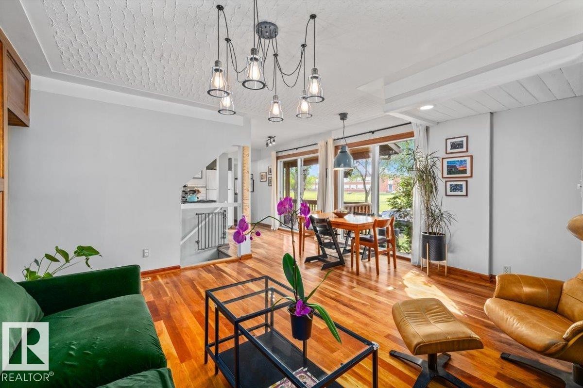 Open-concept living space featuring wood-finish flooring, a contemporary multi-bulb chandelier, large sliding glass doors, and a dining area - 11603 70 Street Nw, Edmonton, AB