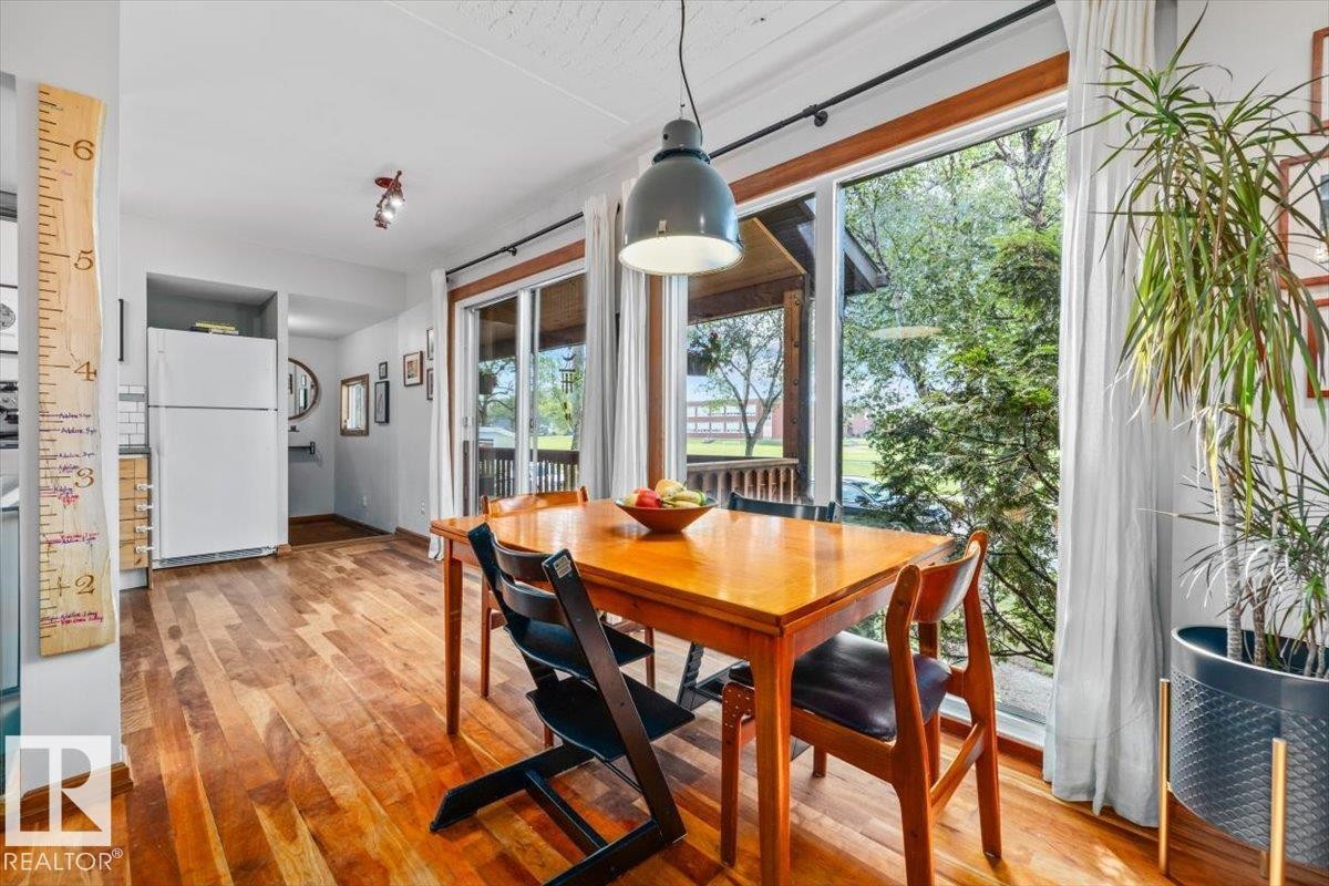 Dining area featuring full-height windows, wood-finish flooring, and a sliding glass door to an outdoor deck - 11603 70 Street Nw, Edmonton, AB