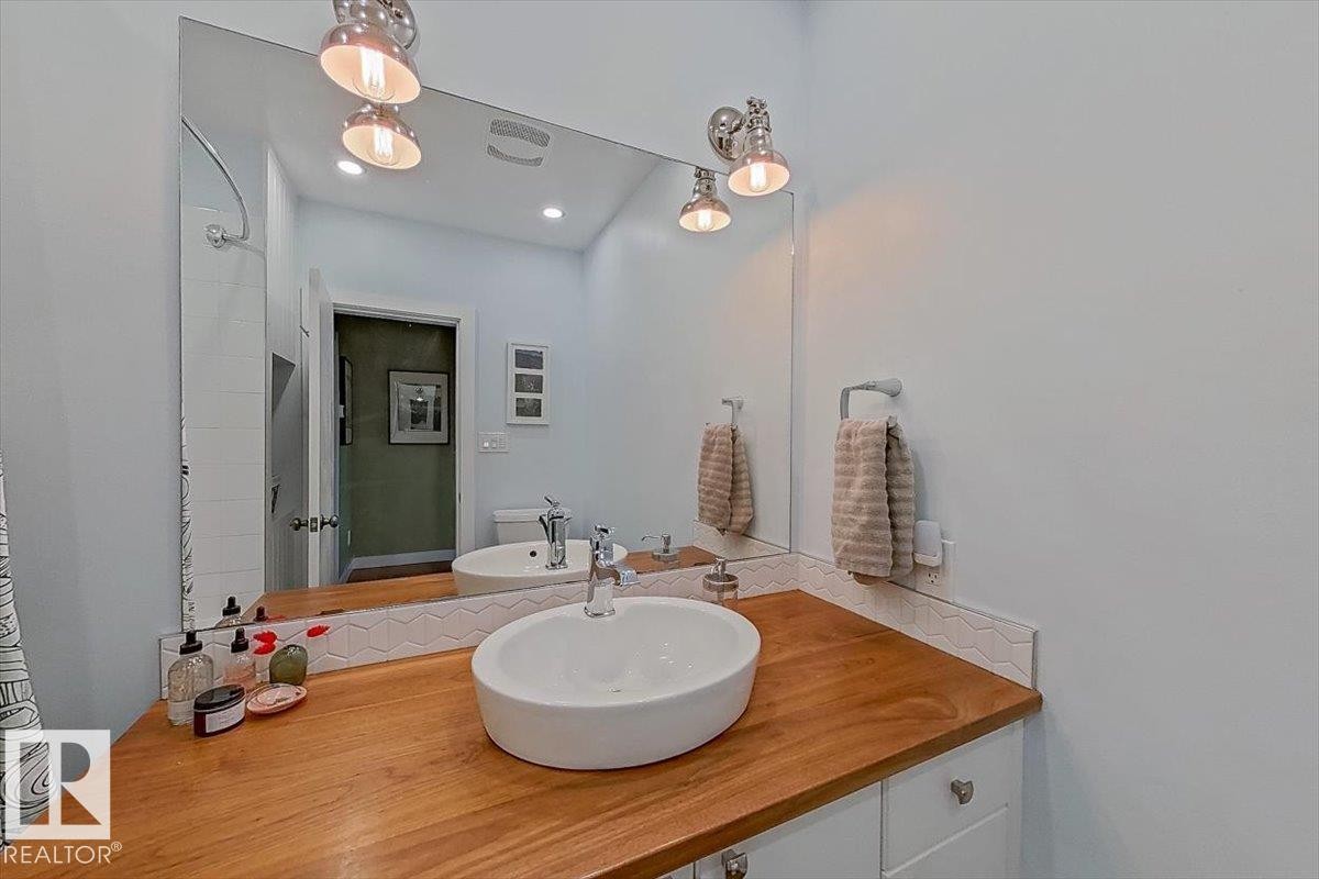Bathroom vanity featuring a vessel sink, wood-finish countertop, and white cabinetry with brushed nickel hardware - 11603 70 Street Nw, Edmonton, AB
