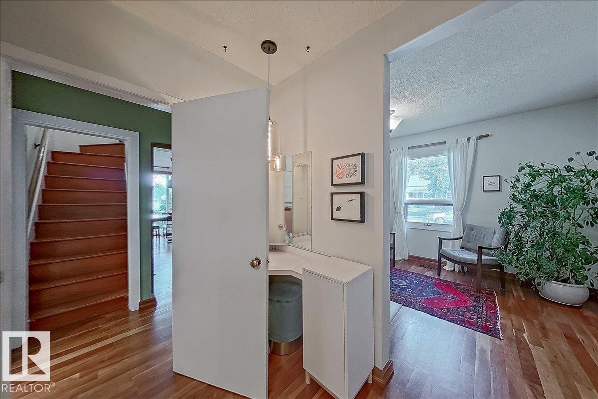 Hardwood flooring throughout the entry area, a built-in vanity with a mirror, a window with natural light, and a wooden staircase - 11603 70 Street Nw, Edmonton, AB