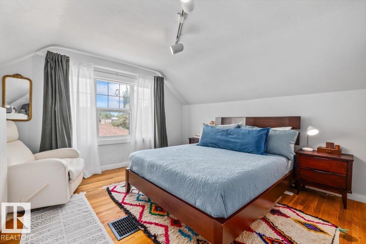 Hardwood flooring throughout, featuring a double window with dual curtain rods and white and grey fabric drapes - 11603 70 Street Nw, Edmonton, AB
