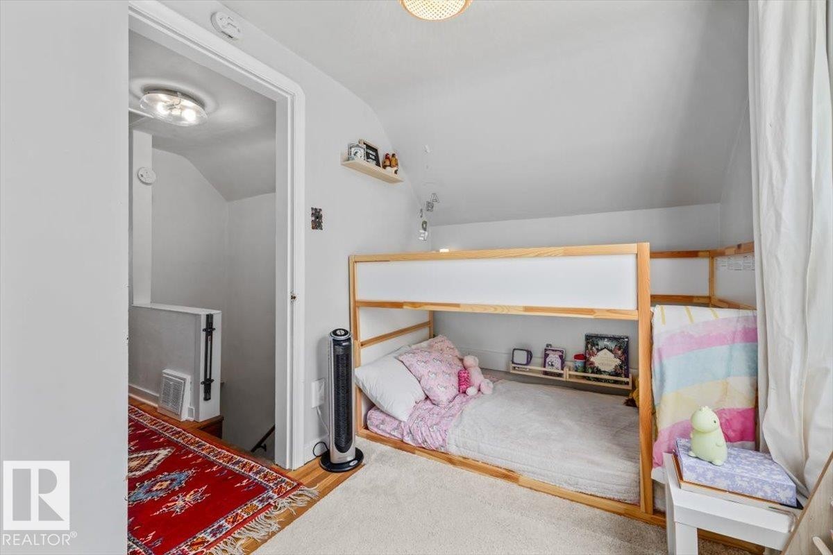 Wood-finish flooring with an intricate area rug complements a white-painted wall and a doorway leading to a staircase with a white half-wall - 11603 70 Street Nw, Edmonton, AB