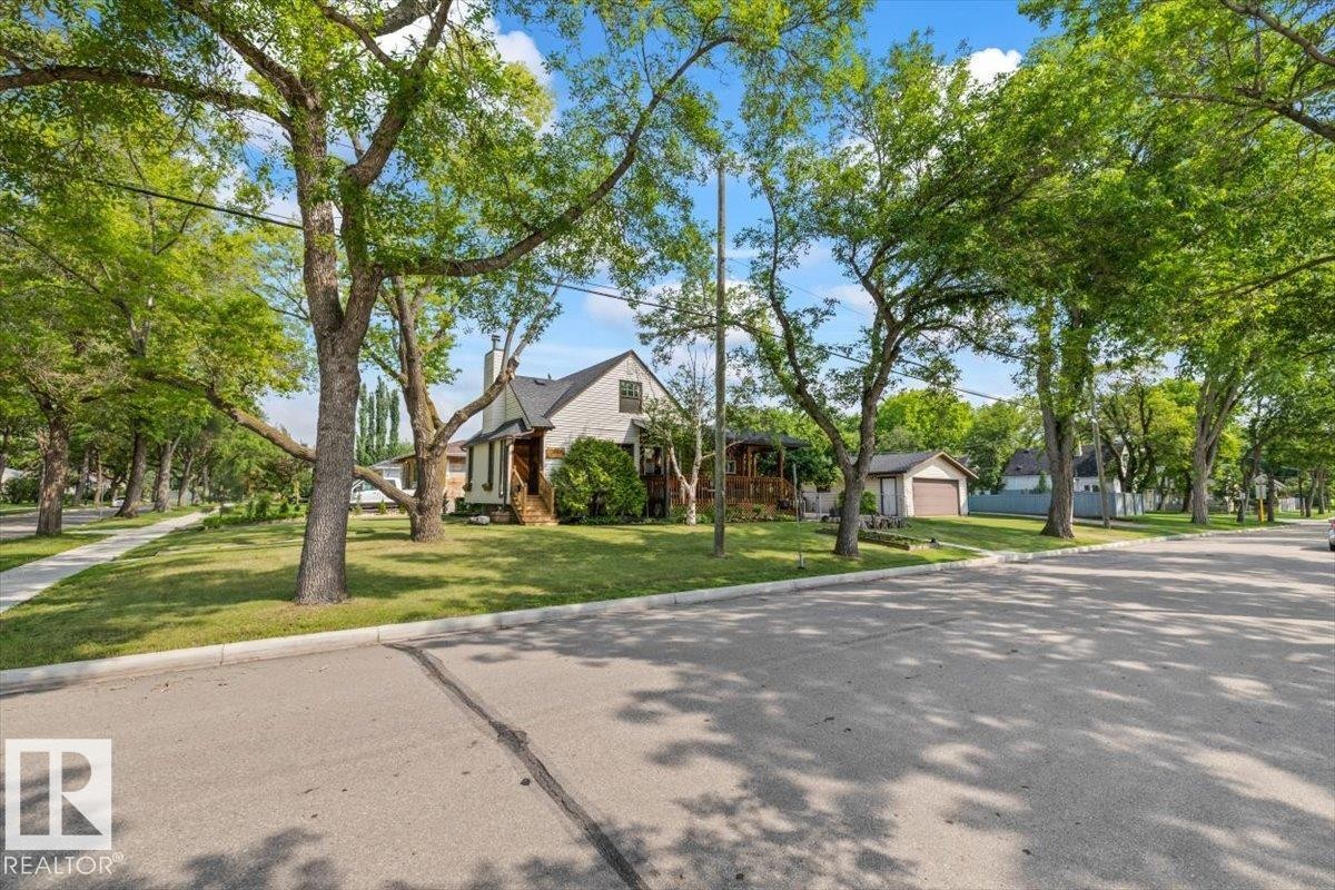 Charming home featuring a pitched roof, front porch, mature trees, manicured lawn, and a detached garage - 11603 70 Street Nw, Edmonton, AB