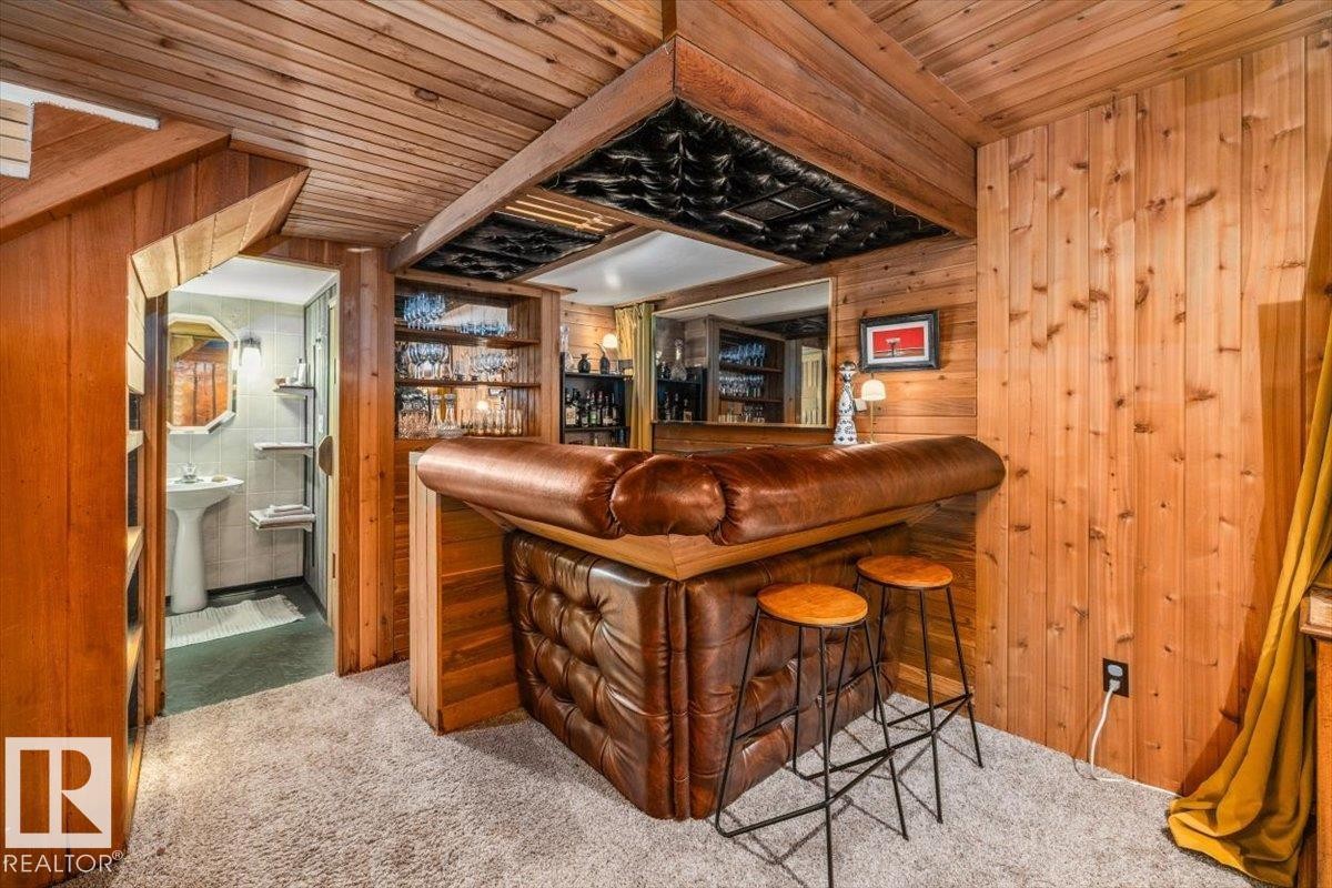 Recreation room featuring extensive wood paneling, a built-in wet bar with tufted leather upholstery, integrated shelving, and carpet flooring - 11603 70 Street Nw, Edmonton, AB