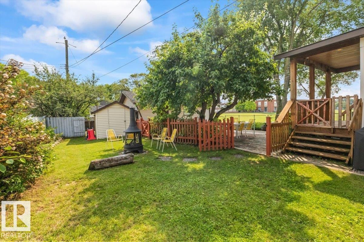 Fenced backyard featuring a covered wooden deck, stone patio, mature trees, and a storage shed - 11603 70 Street Nw, Edmonton, AB