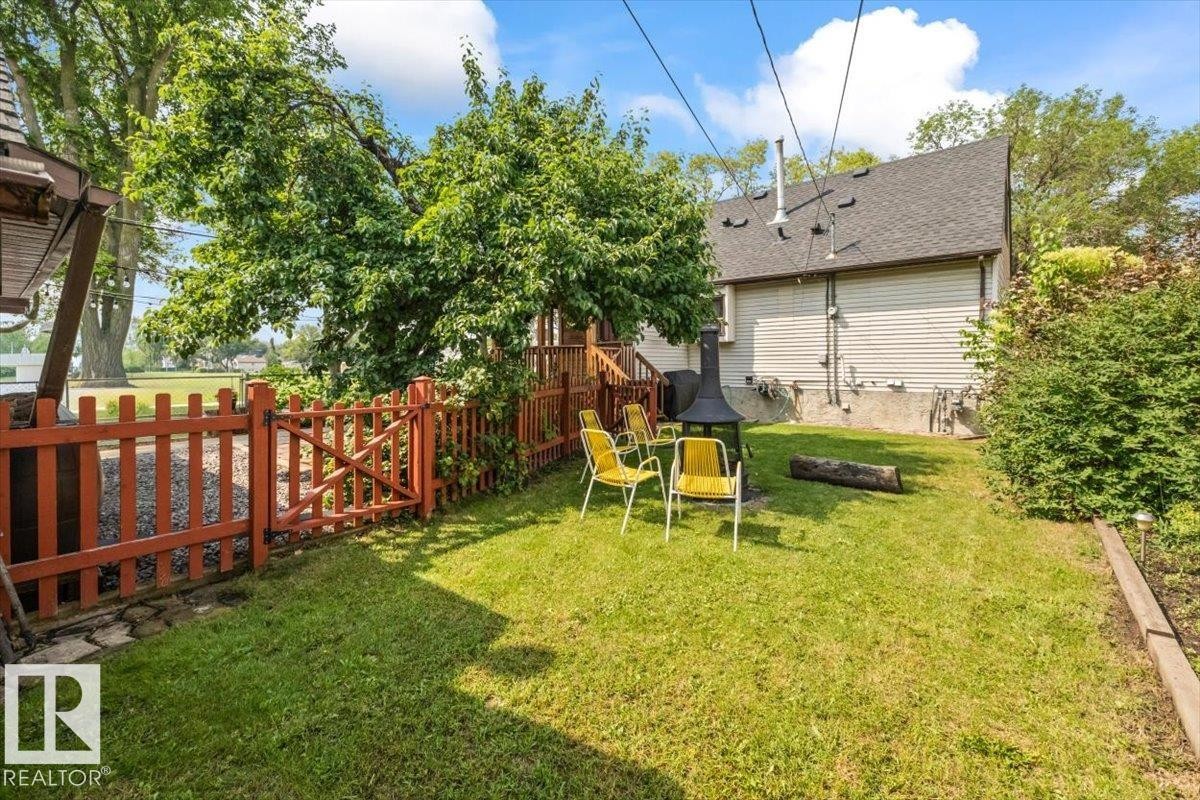 Grassed backyard featuring a wooden picket fence, mature trees, a raised garden bed, and a partial view of the property's exterior siding - 11603 70 Street Nw, Edmonton, AB