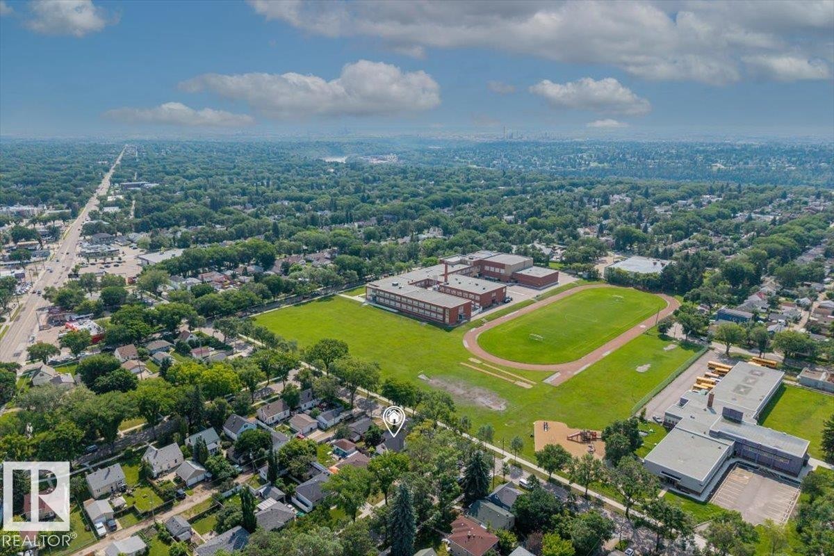 Aerial perspective showcasing a residential neighborhood with extensive tree canopies, featuring a prominent school building with athletic fields and a track - 11603 70 Street Nw, Edmonton, AB