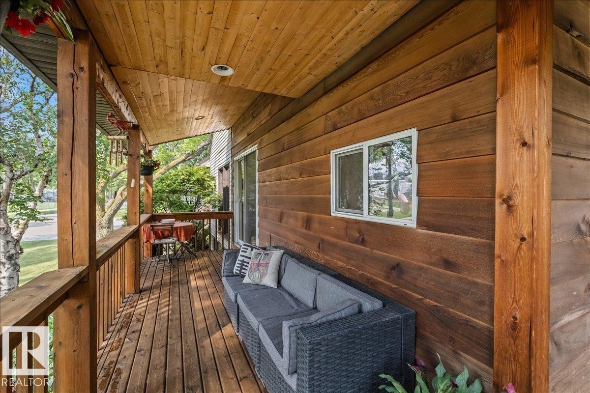 Wood-paneled covered porch featuring a wood-plank floor, exposed wood beams, and a sliding glass door - 11603 70 Street Nw, Edmonton, AB