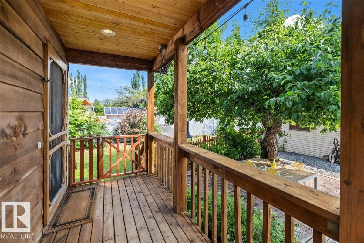 Covered wood-plank deck with a full wood railing system, leading to a fenced yard with mature trees and a gravel patio area - 11603 70 Street Nw, Edmonton, AB