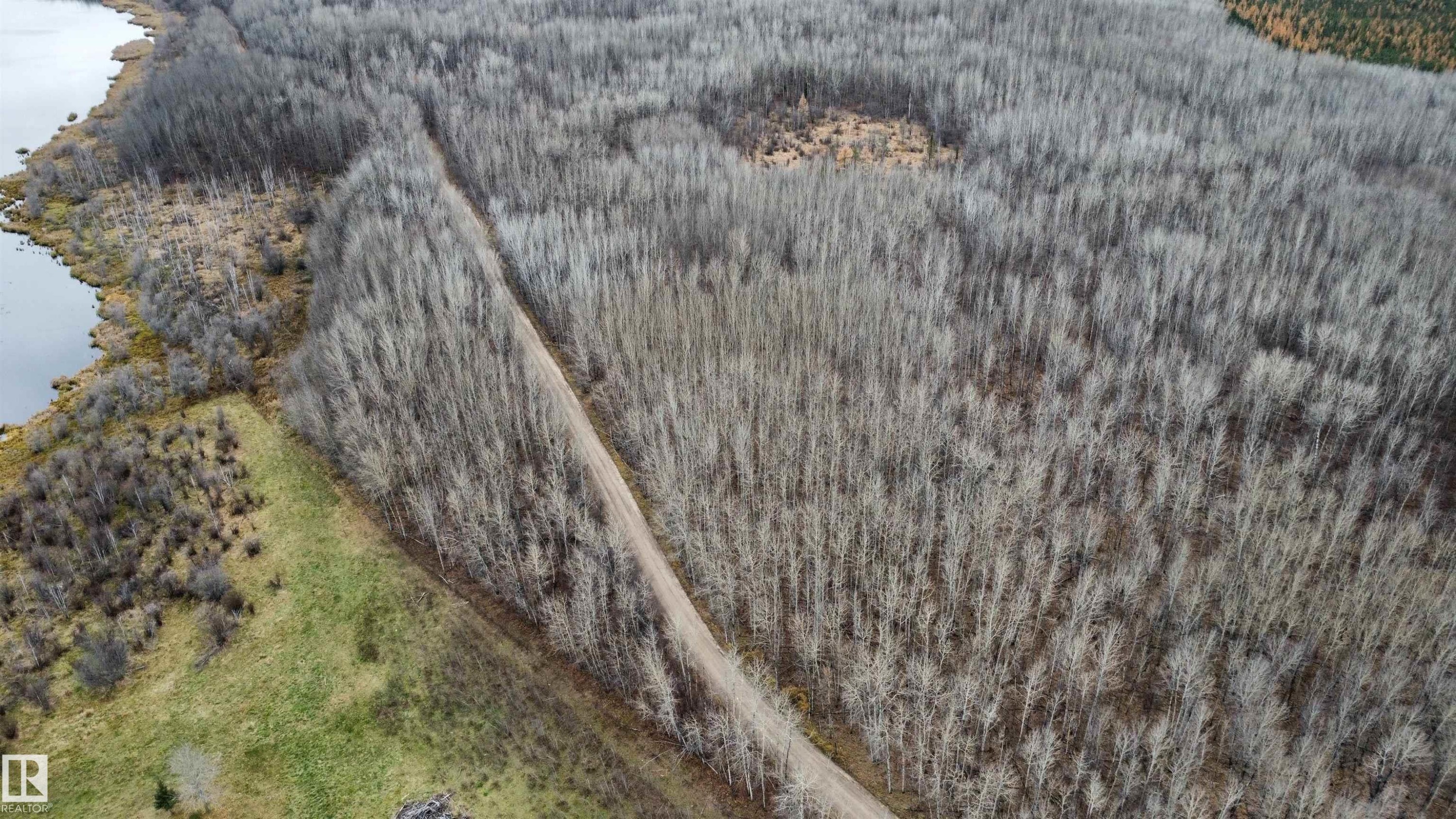 Expansive wooded acreage featuring a natural water body boundary and a defined dirt trail - Rge Rd 62, Rural Barrhead County, AB