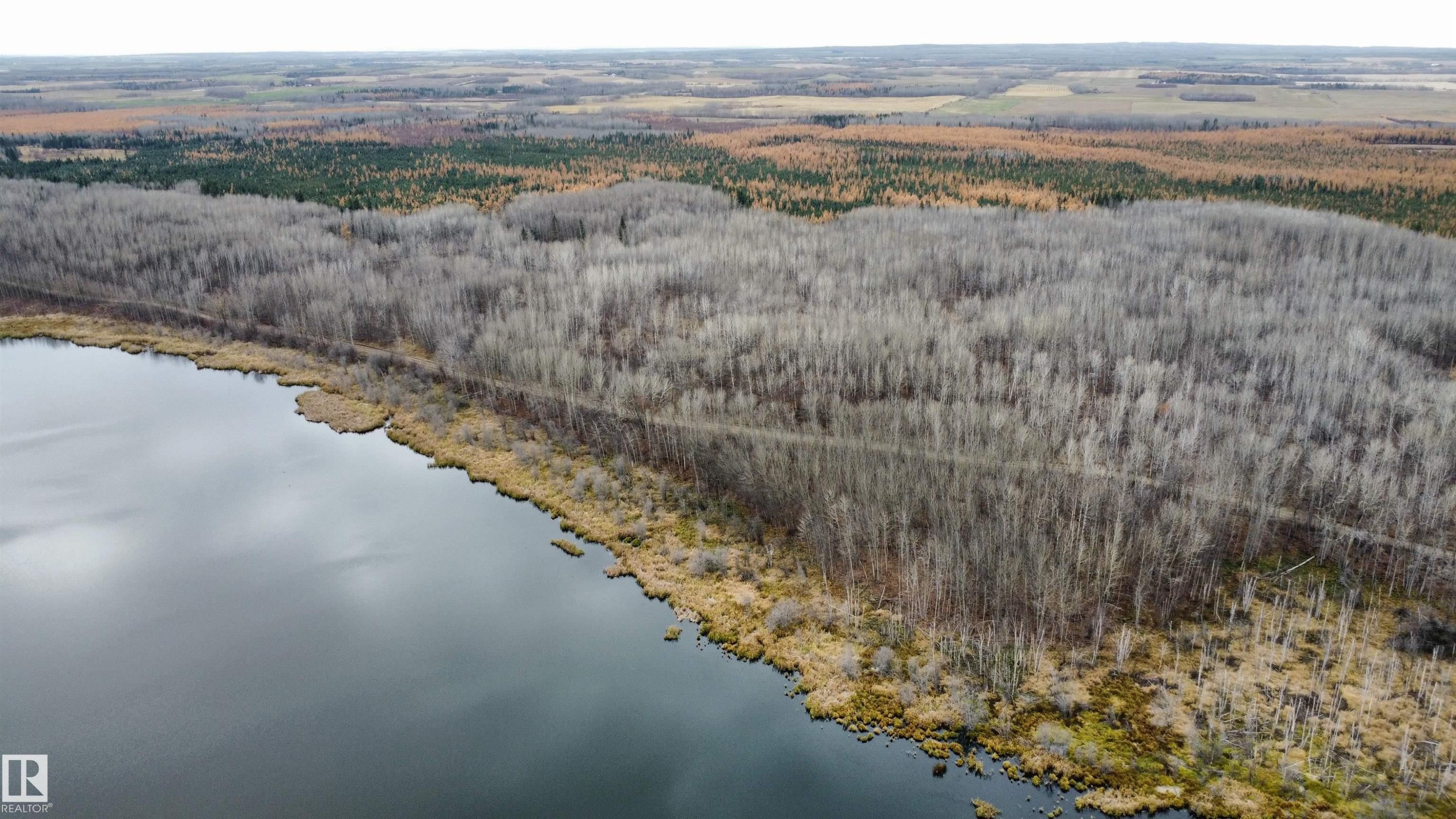 Expansive aerial overview showcasing a serene body of water, dense woodland, and a distant treeline - Rge Rd 62, Rural Barrhead County, AB