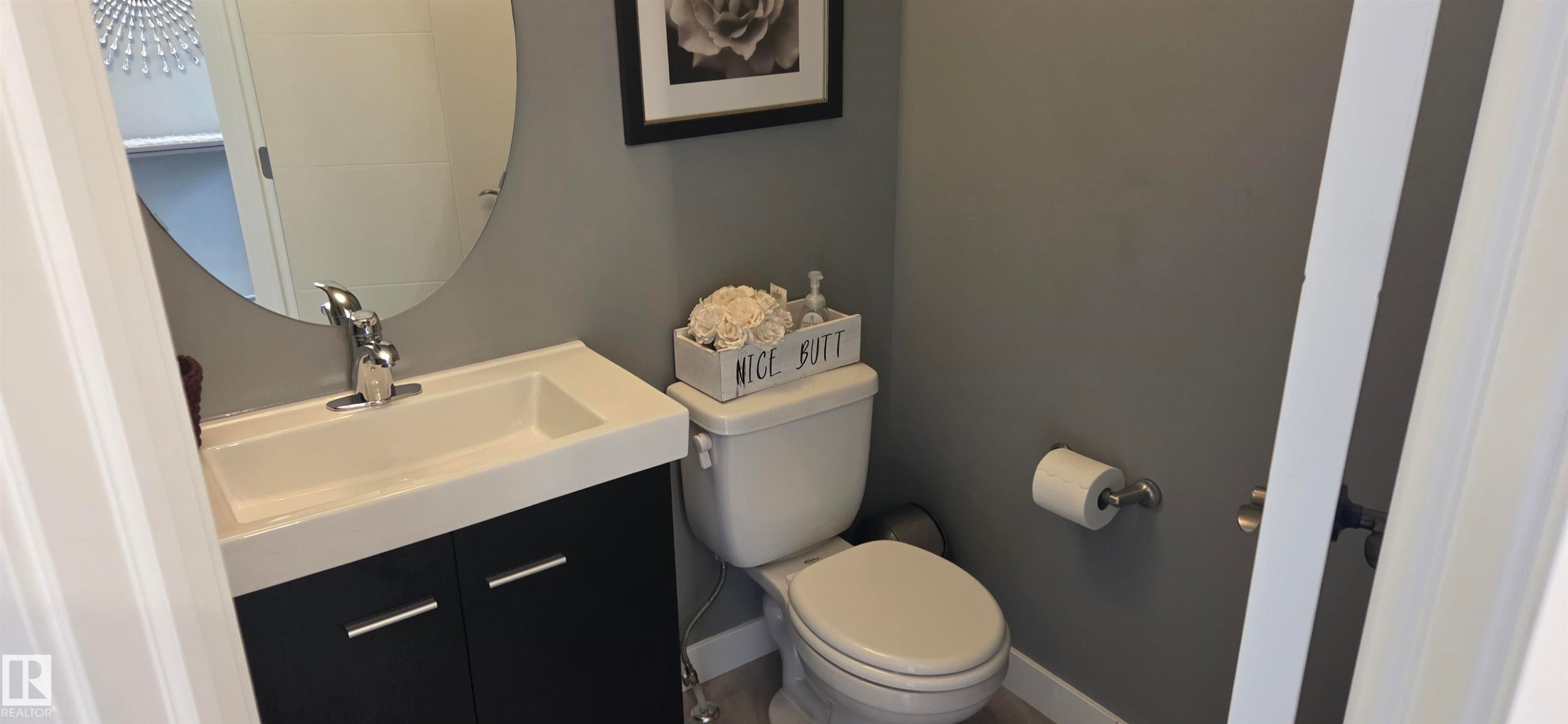 Compact bathroom featuring a white toilet, contemporary vanity with a chrome faucet, and a round wall mirror - 16505 133 Street, Edmonton, AB