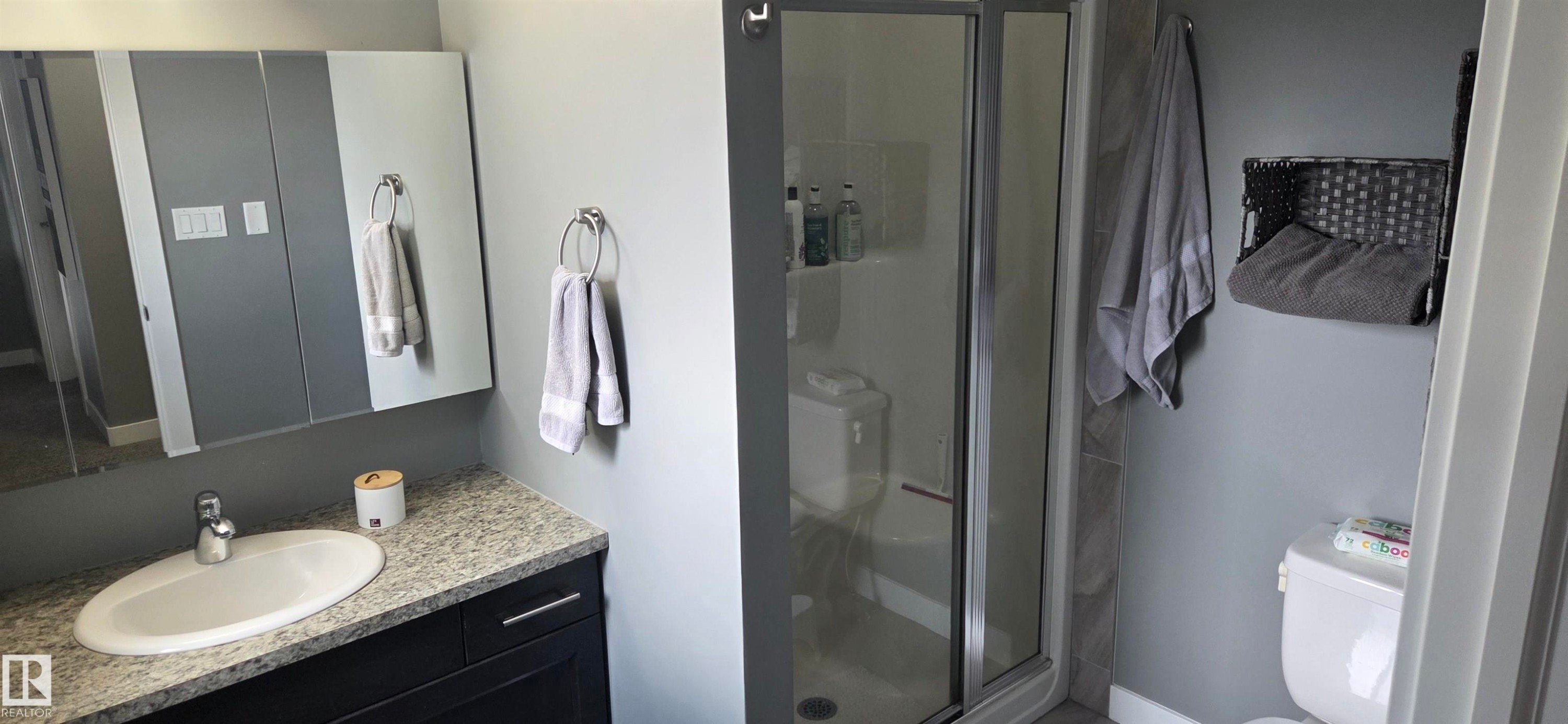 Bathroom featuring a granite-look countertop, undermount sink, dark wood-finish vanity, and a glass-enclosed shower - 16505 133 Street, Edmonton, AB
