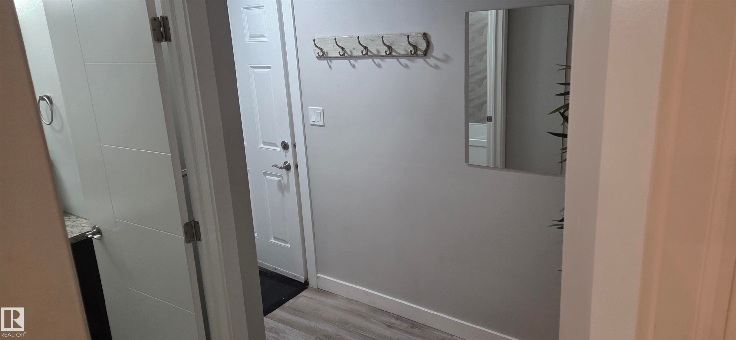 Entryway featuring wood-finish flooring, a white paneled door, and a wall-mounted coat rack - 16505 133 Street, Edmonton, AB