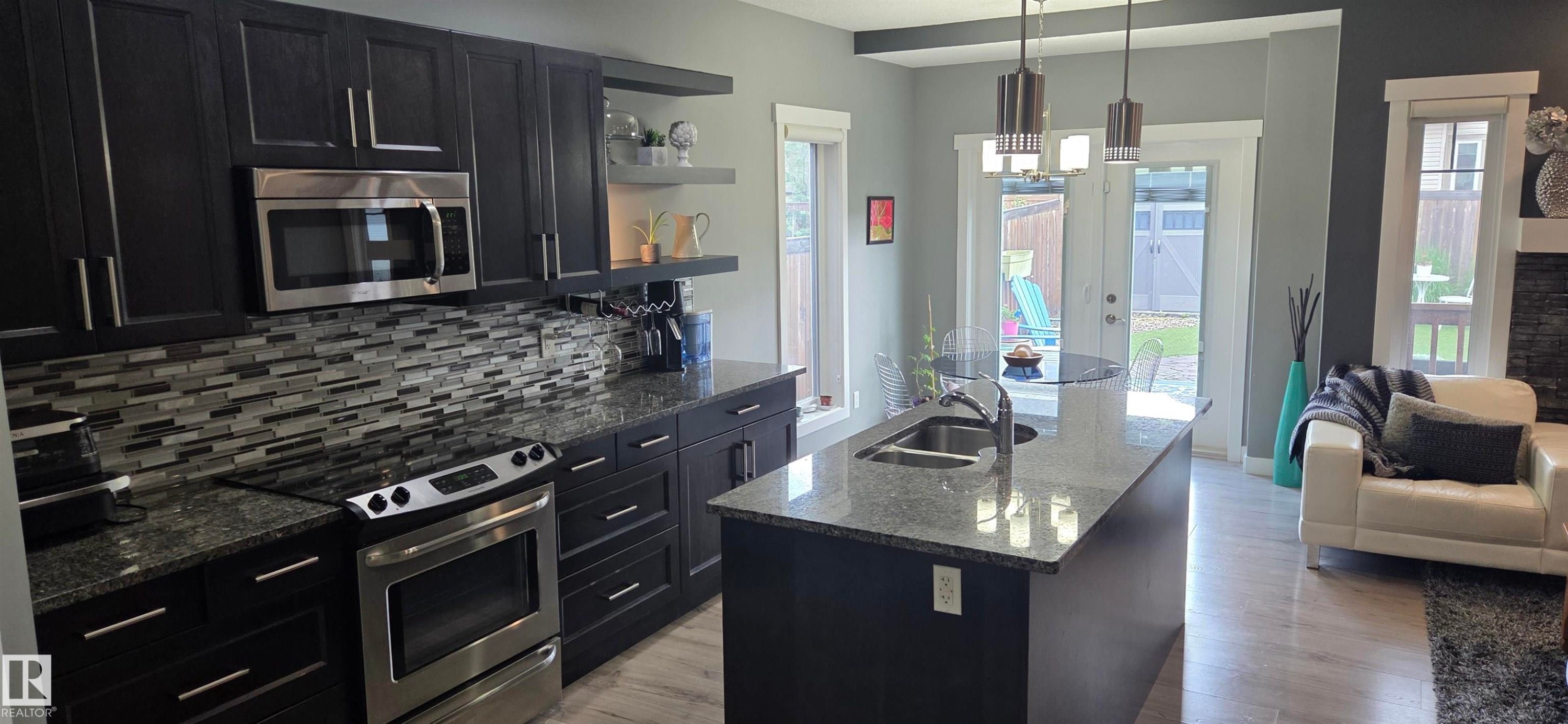 Modern kitchen featuring dark cabinetry, stainless steel appliances, and granite countertops - 16505 133 Street, Edmonton, AB