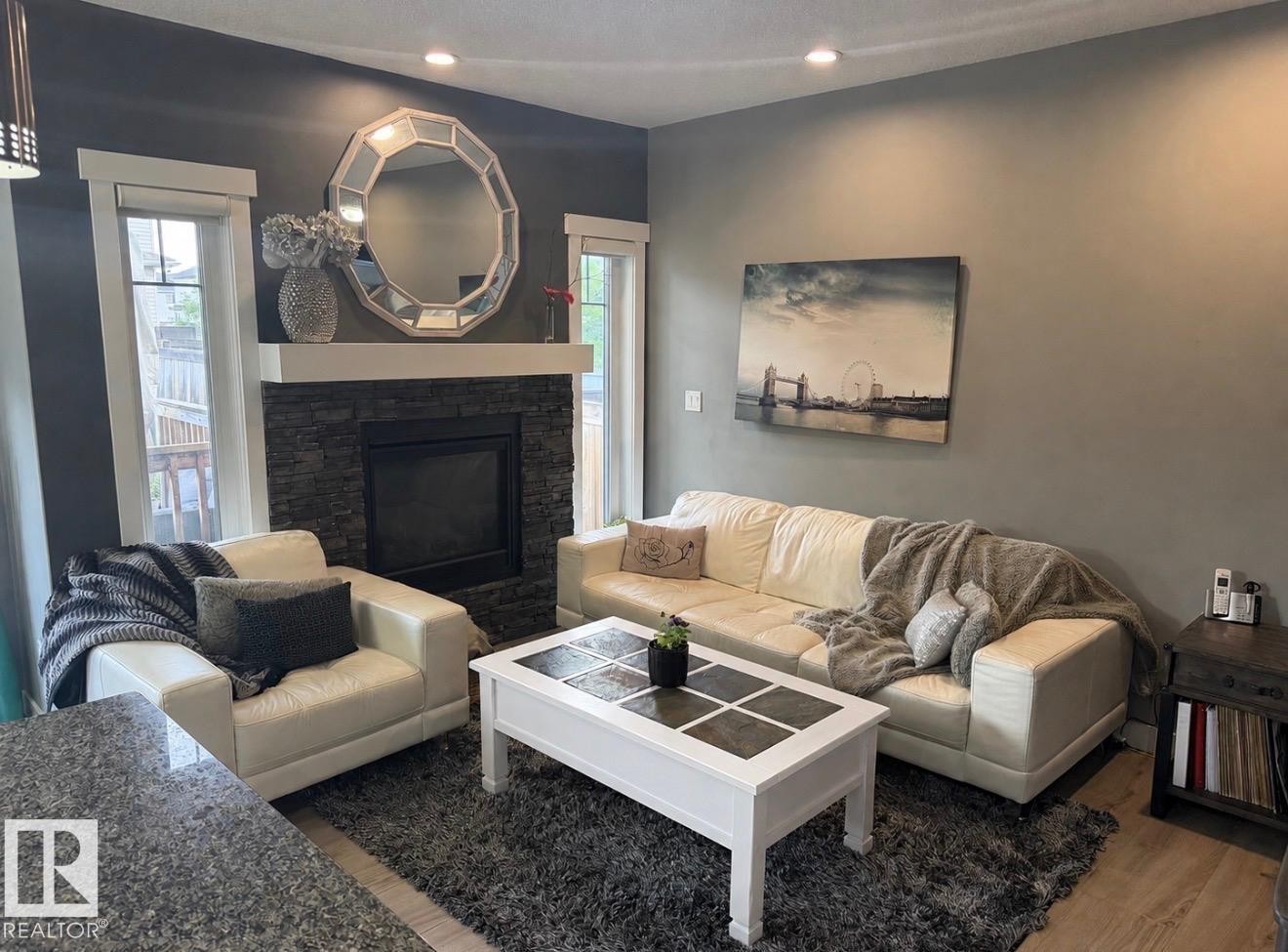 Living area featuring a stacked stone fireplace with a white mantel, recessed lighting, and light wood-finish flooring - 16505 133 Street, Edmonton, AB