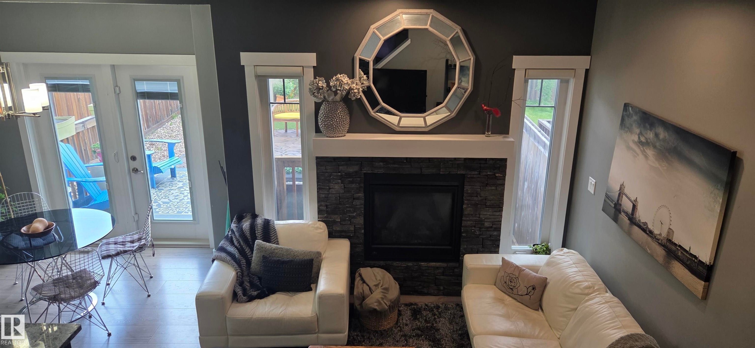 Living area featuring a floor-to-ceiling stone fireplace with a white mantel, complemented by a large octagonal mirror - 16505 133 Street, Edmonton, AB