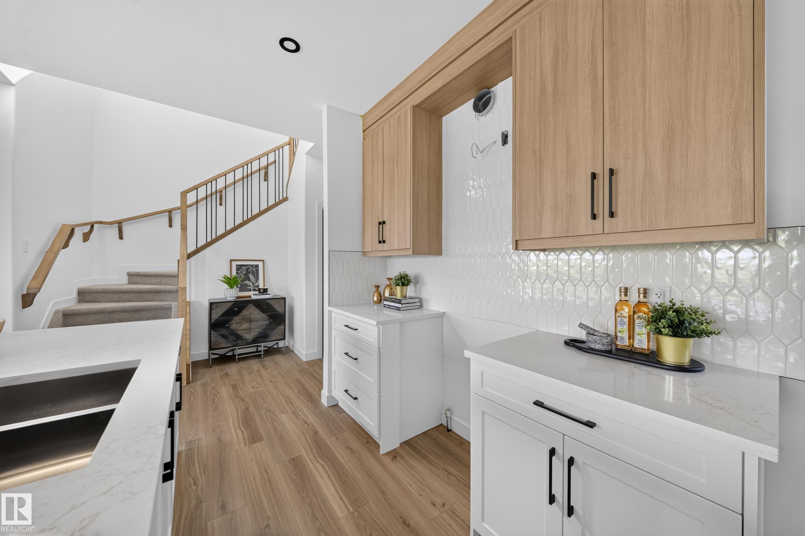 Contemporary kitchen with light wood-finish upper cabinetry, white lower cabinetry, and black hardware - 523 Ashgrove Circle, Leduc, AB