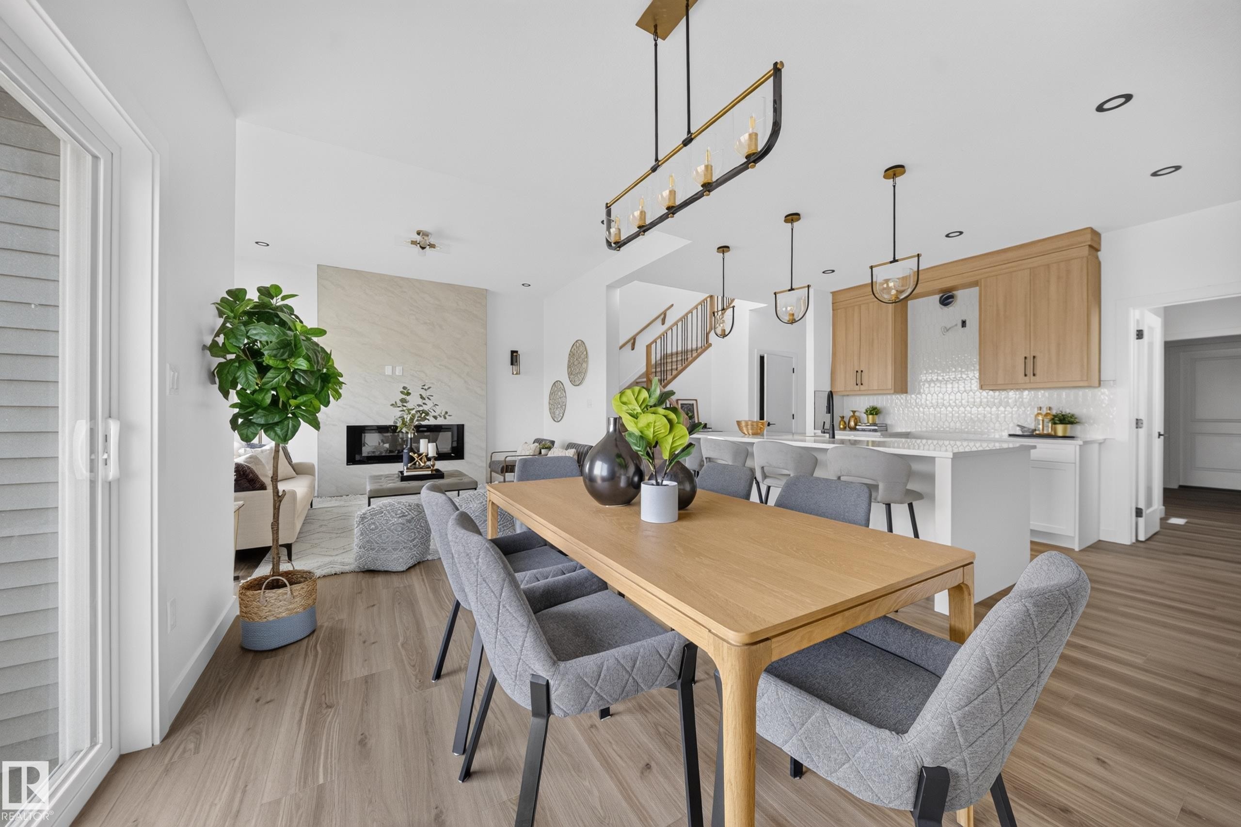 Open-concept living area featuring wood-finish flooring, a contemporary linear fireplace with a stone surround, and a kitchen with light wood cabinetry and a white tiled backsplash - 523 Ashgrove Circle, Leduc, AB