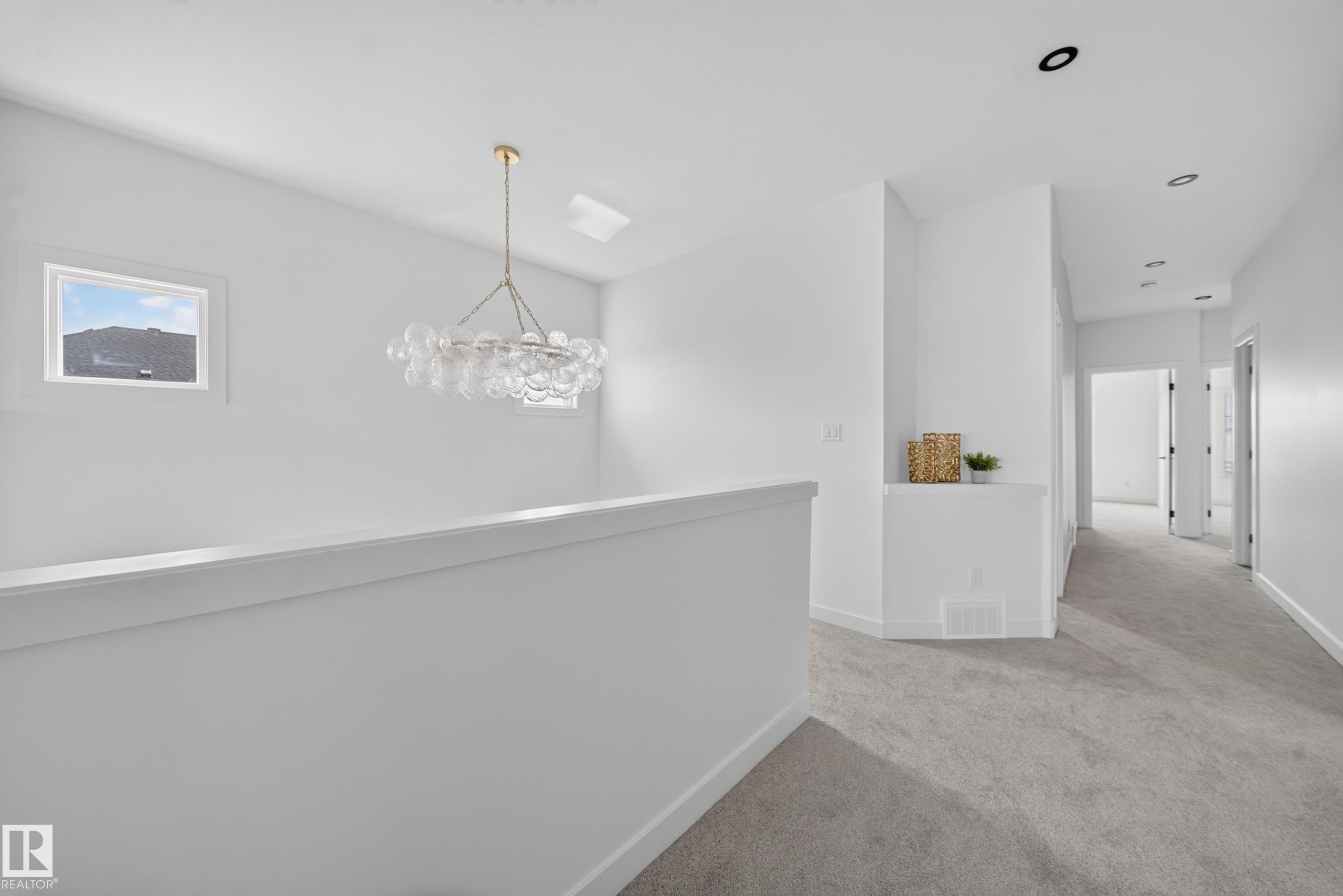 Upper-level hallway featuring a contemporary chandelier, recessed lighting, and light gray carpeting - 523 Ashgrove Circle, Leduc, AB
