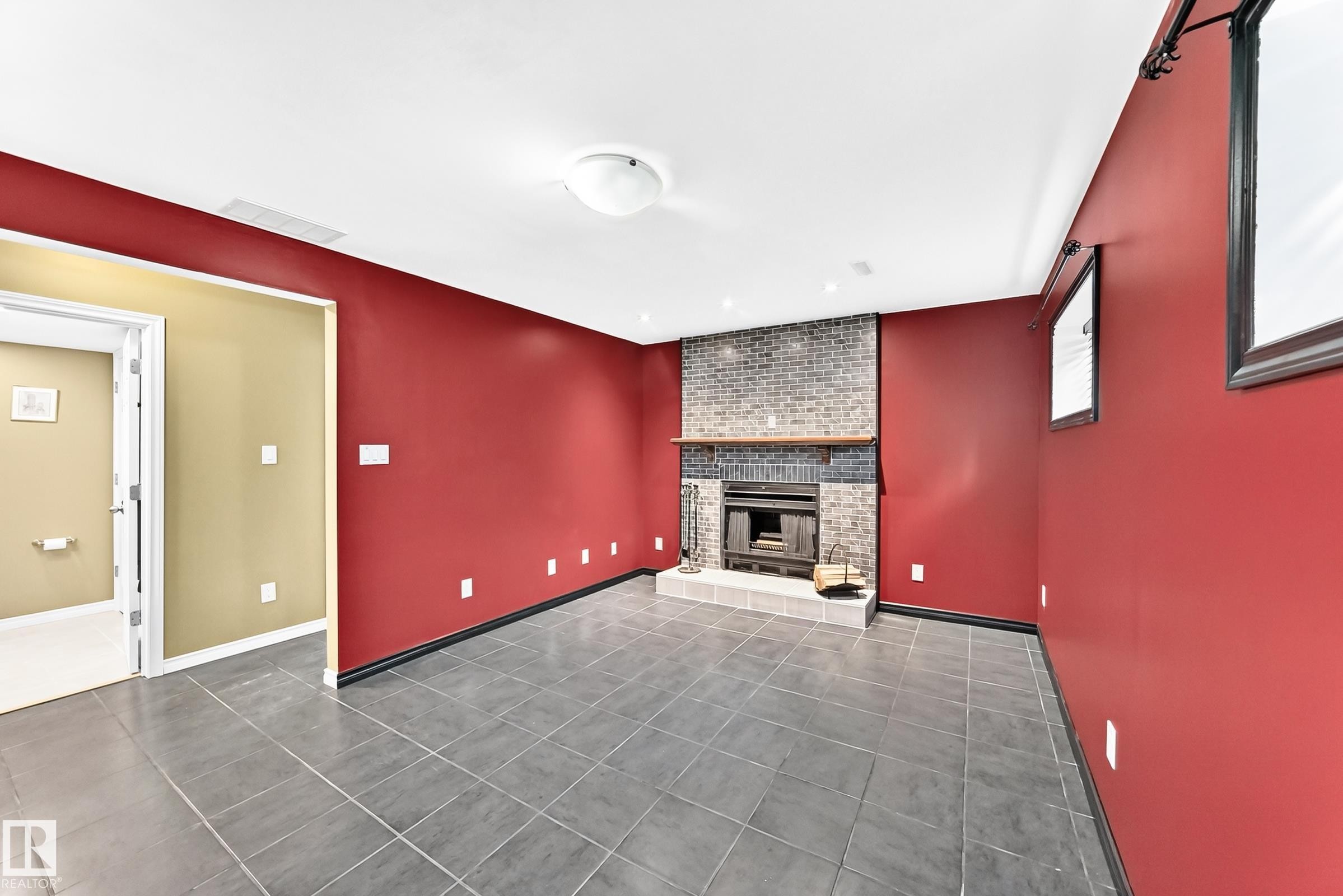 Spacious room featuring a brick fireplace with a wood mantel, dark gray tile flooring, and a neutral ceiling with a flush-mount light fixture - 1763 48A Street, Edmonton, AB