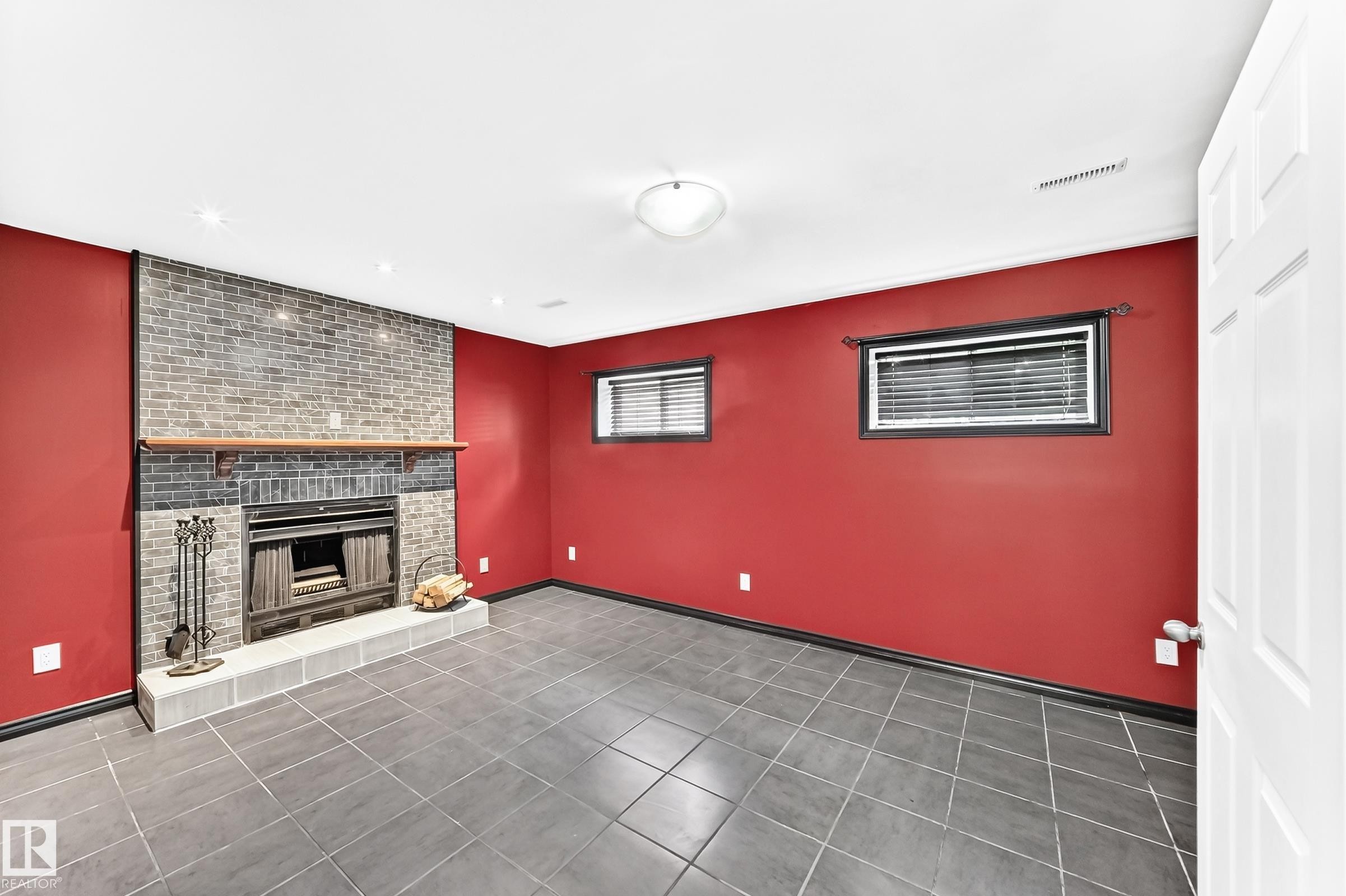 Spacious room featuring a brick fireplace with a wood mantle, tile hearth, and dark grey tile flooring - 1763 48A Street, Edmonton, AB
