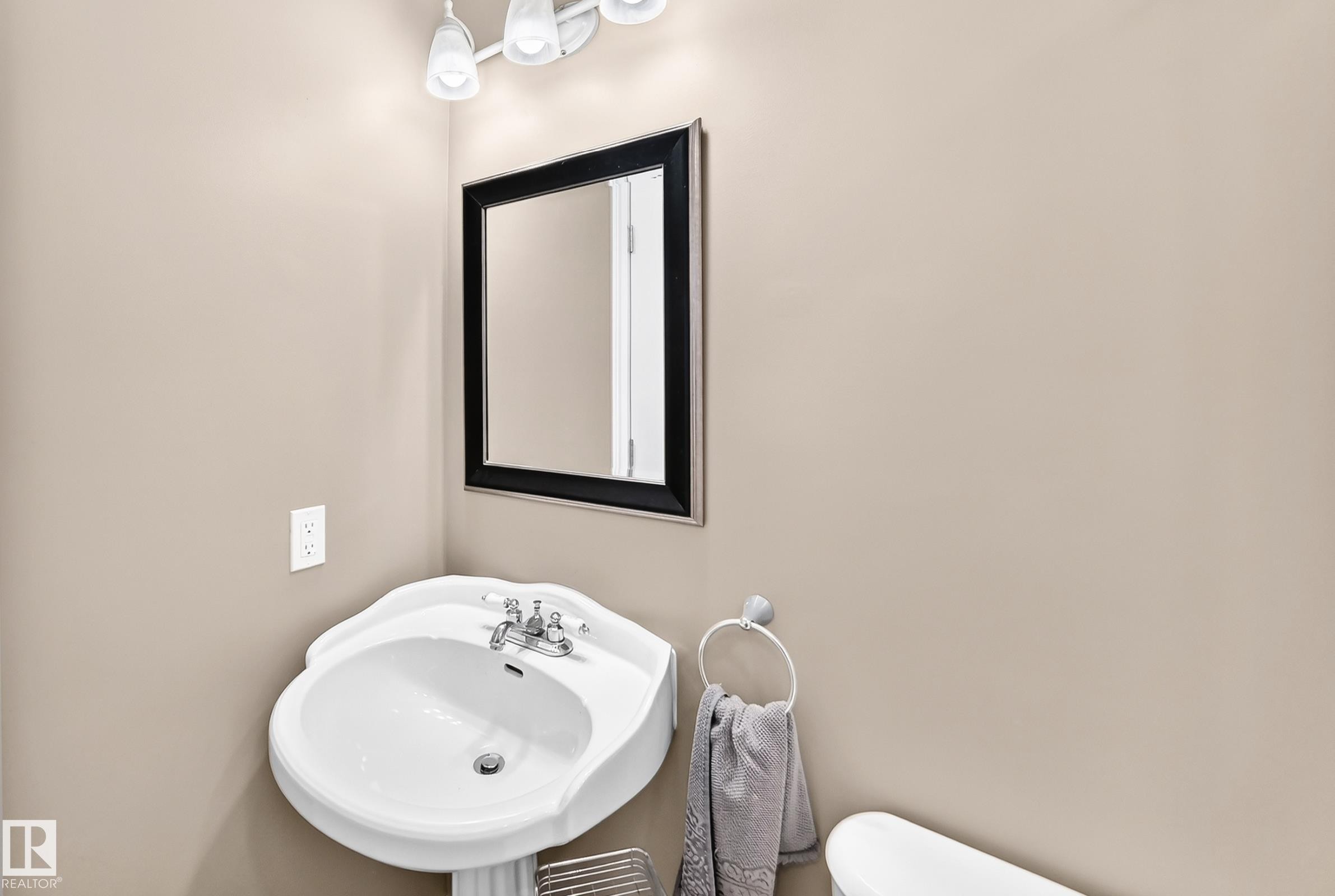 Pedestal sink with chrome fixtures, framed mirror, and wall-mounted light fixture - 1763 48A Street, Edmonton, AB