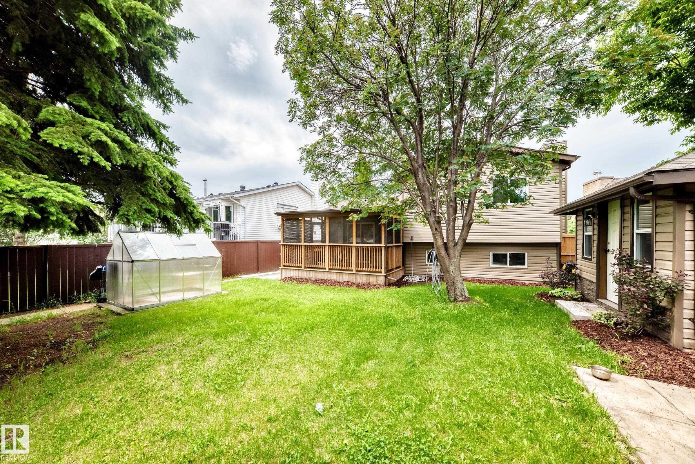 Expansive backyard with a manicured lawn, screened porch, and dedicated greenhouse structure - 1763 48A Street, Edmonton, AB