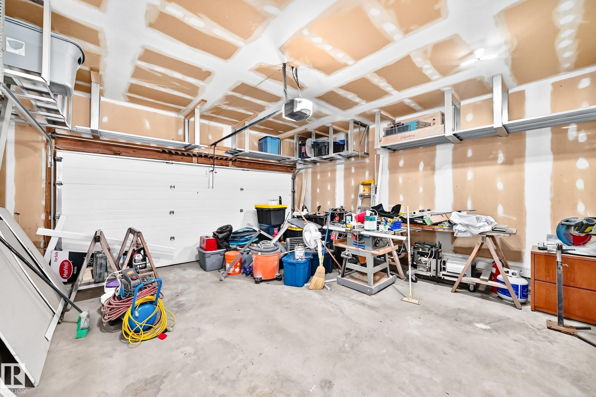 Spacious garage featuring a concrete floor, exposed ceiling joists, and multiple overhead storage racks - 1763 48A Street, Edmonton, AB