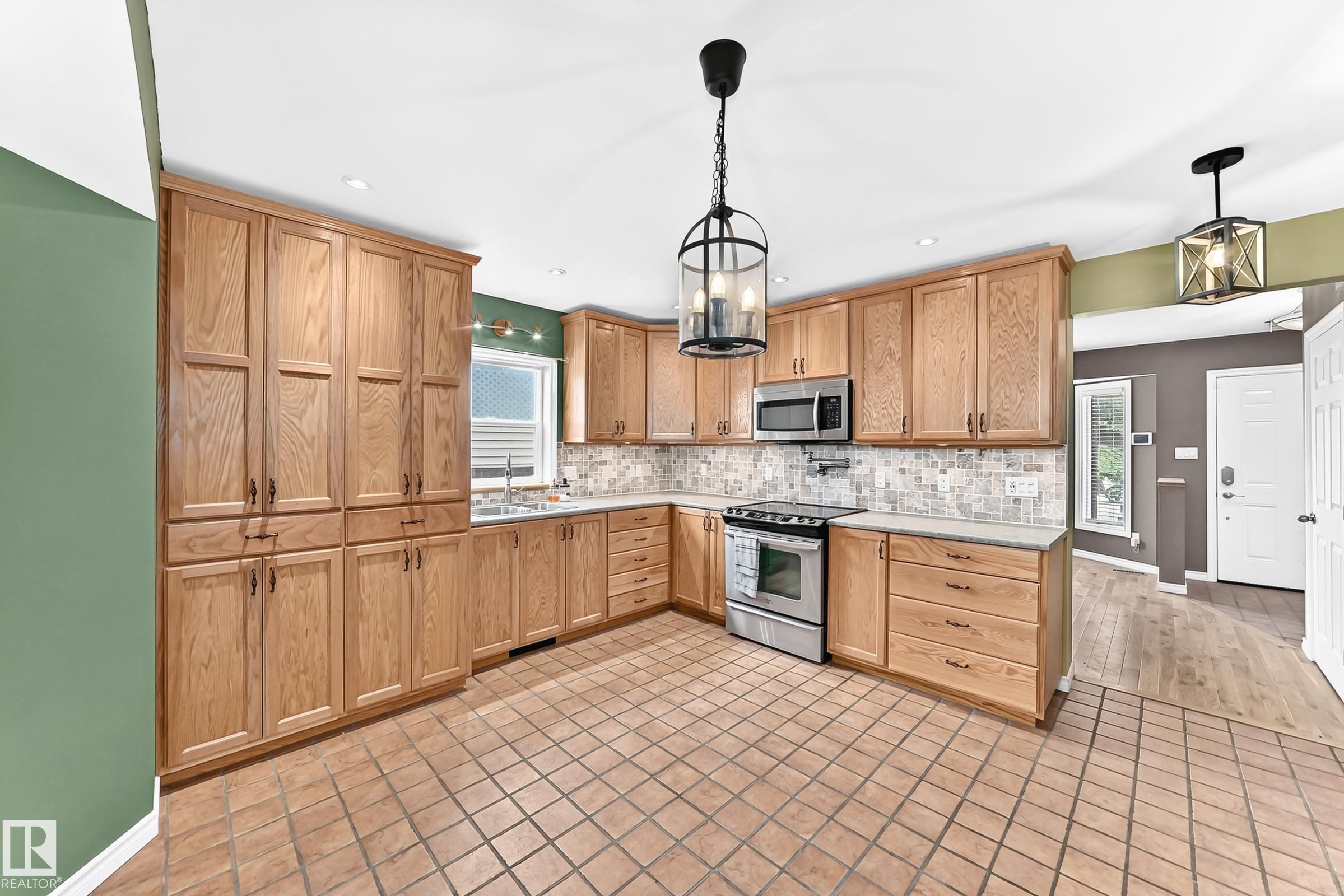 Kitchen featuring extensive wood cabinetry, stainless steel appliances, tile flooring, and a patterned tile backsplash - 1763 48A Street, Edmonton, AB
