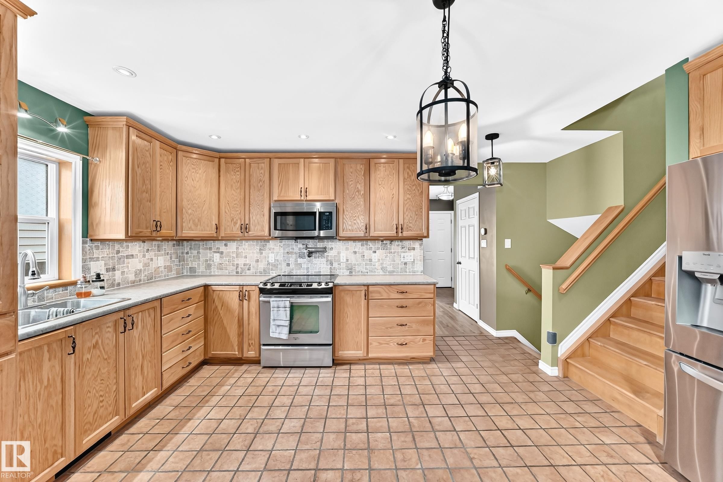 Kitchen featuring light wood cabinetry, stainless steel appliances, and a mosaic tile backsplash - 1763 48A Street, Edmonton, AB