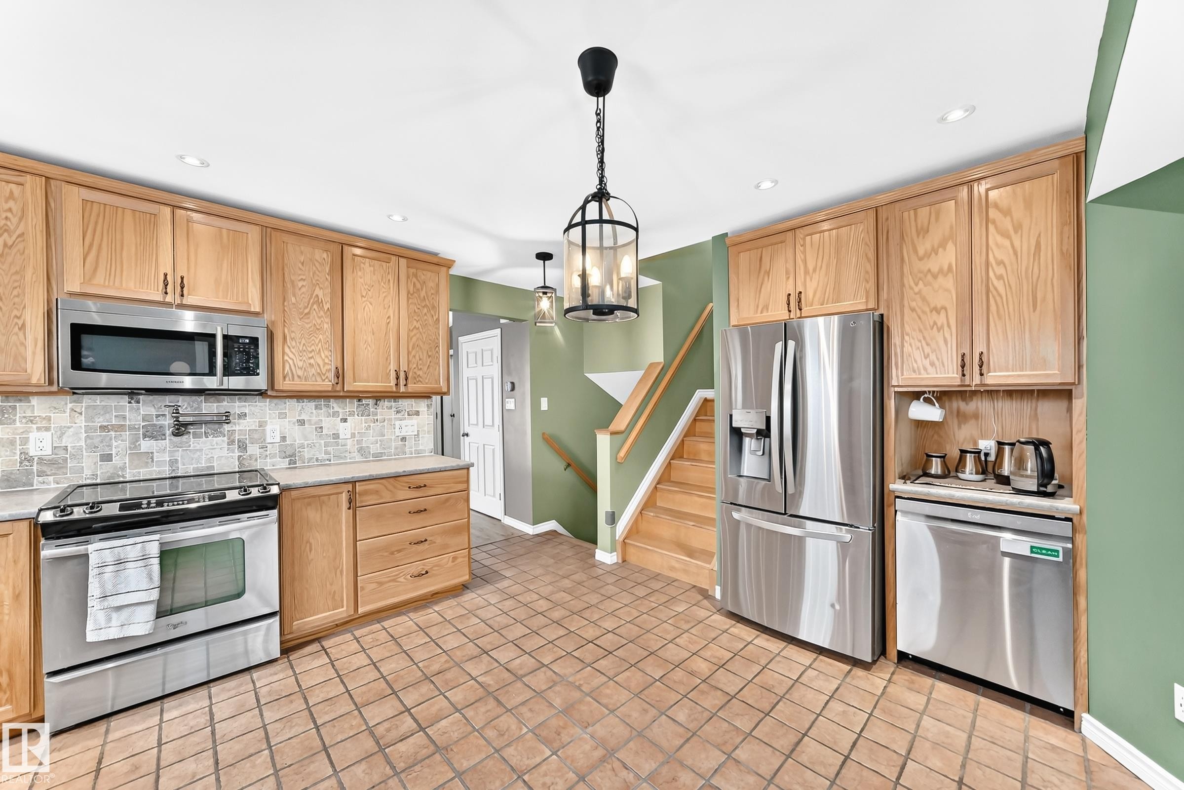 Kitchen featuring stainless steel appliances, light wood-finish cabinetry, tile flooring, and a decorative backsplash - 1763 48A Street, Edmonton, AB