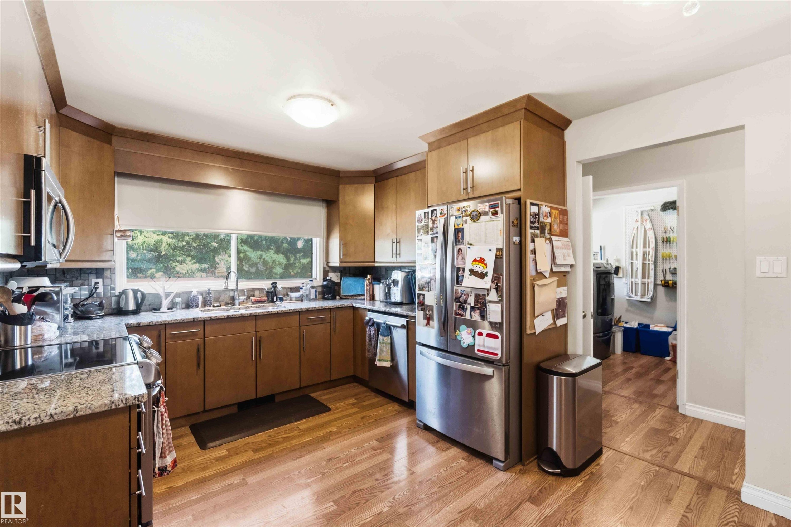 Kitchen featuring wood cabinetry, granite-look countertops, stainless steel appliances, and wood-finish flooring - 13121 122 Street, Edmonton, AB