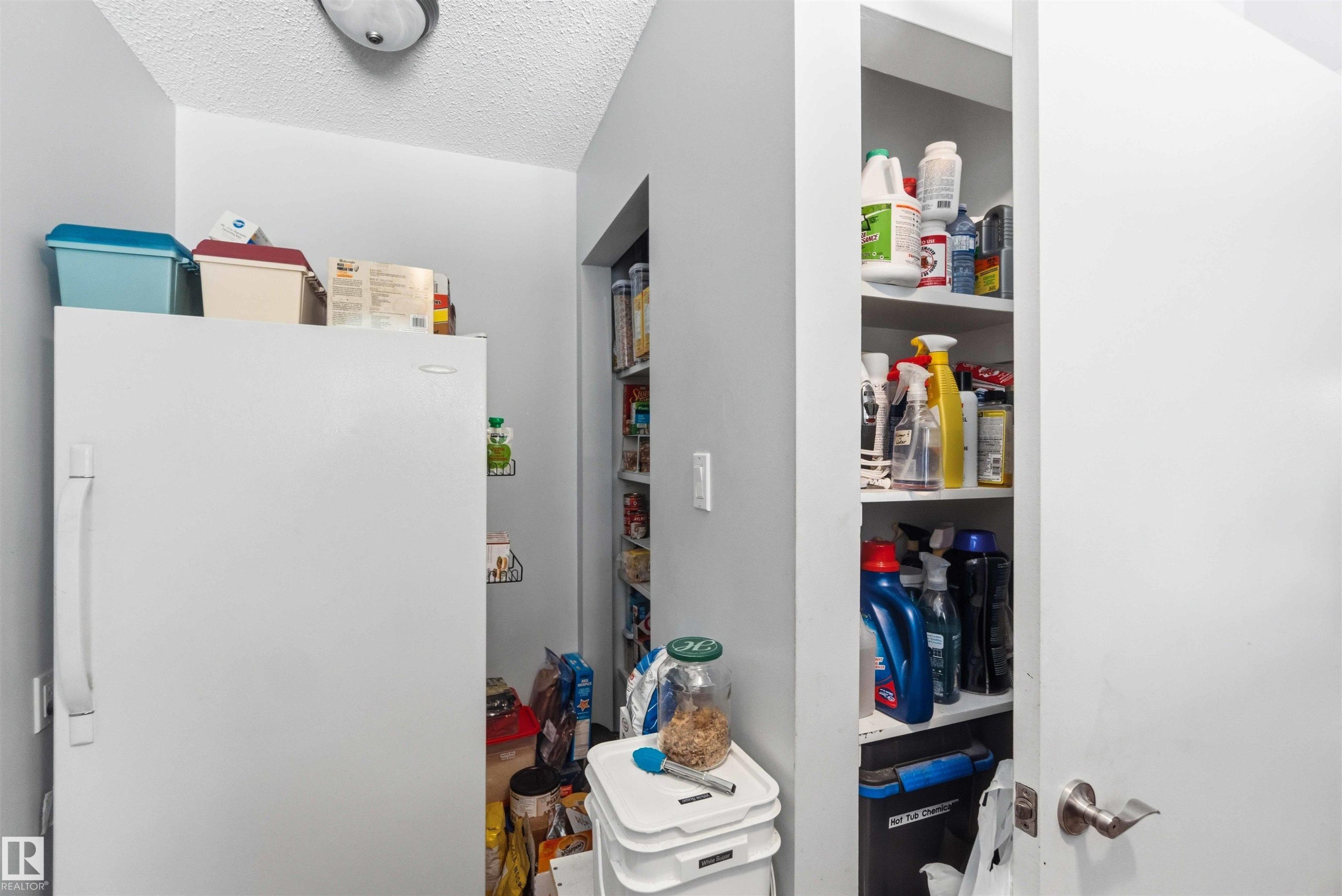 Dedicated utility space featuring a built-in shelving unit, overhead lighting, and a white door with a brushed nickel handle - 13121 122 Street, Edmonton, AB