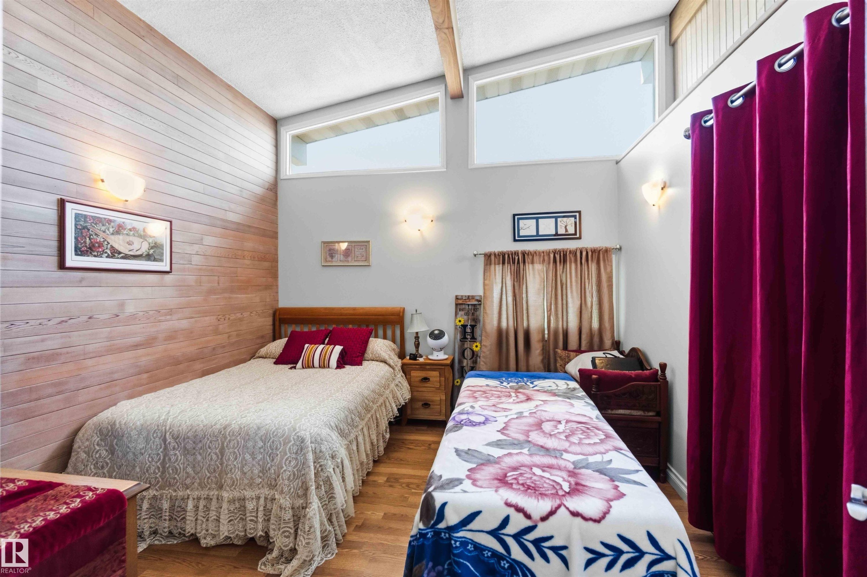 Vaulted ceiling room featuring wood-finish flooring, a plank accent wall, and high transom windows - 13121 122 Street, Edmonton, AB