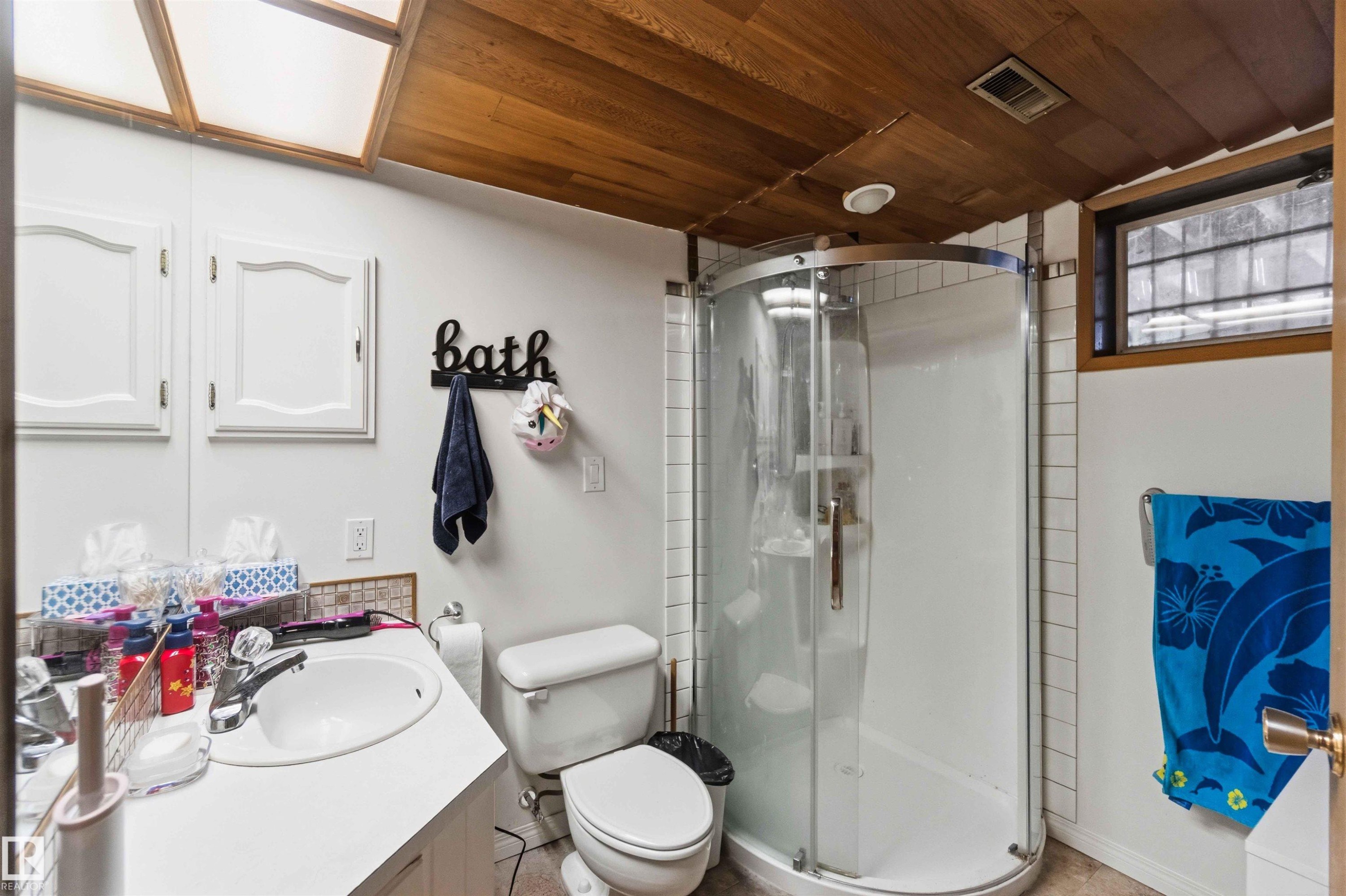Bathroom featuring a walk-in shower with a curved glass enclosure, a single vanity with a white countertop, and a wood-finish ceiling - 13121 122 Street, Edmonton, AB