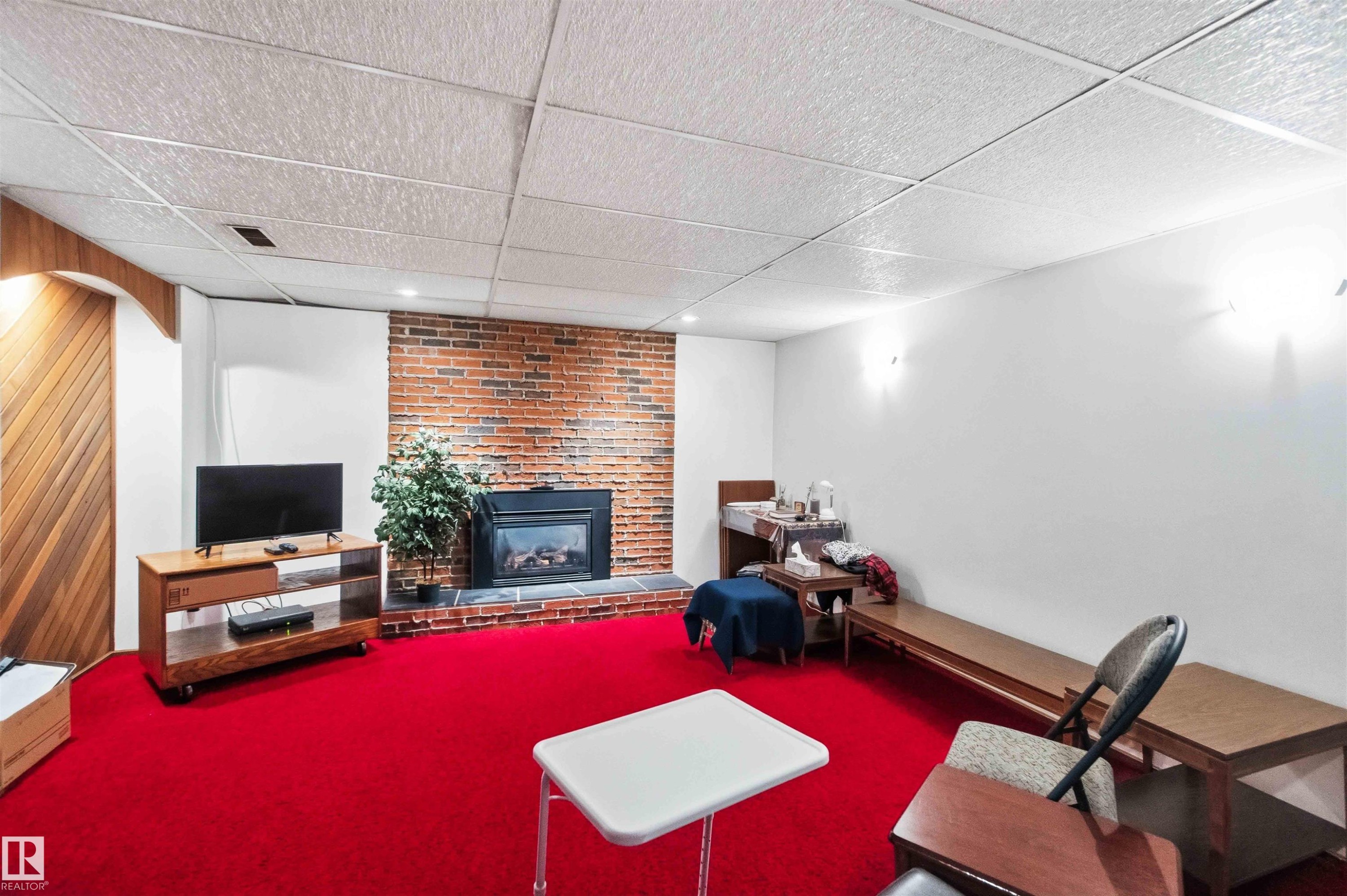 Spacious room with a red carpet flooring and a brick accent wall with a built-in fireplace - 13121 122 Street, Edmonton, AB