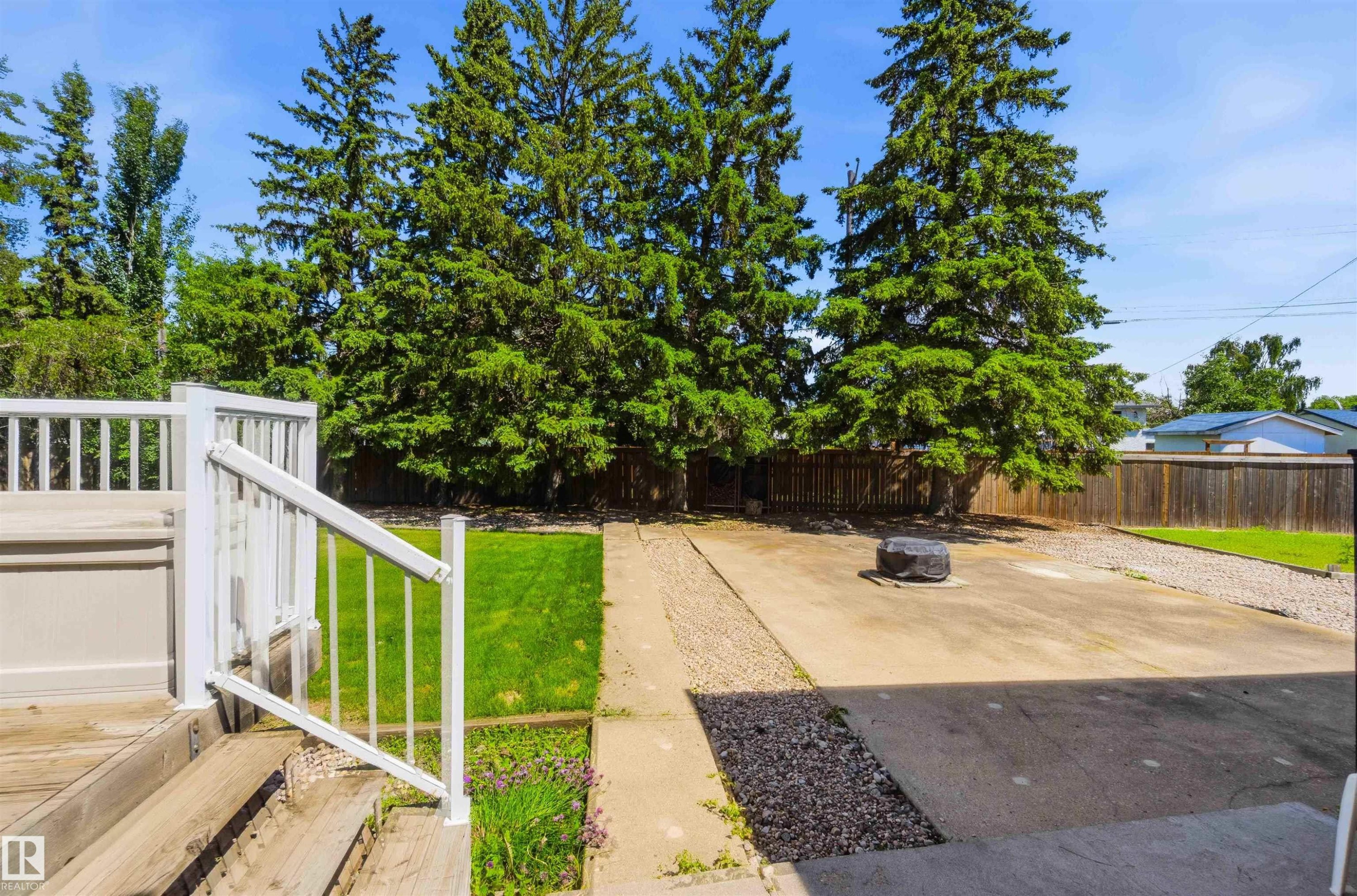 Rear exterior featuring a spacious concrete patio, a section of manicured lawn, and mature trees providing privacy - 13121 122 Street, Edmonton, AB