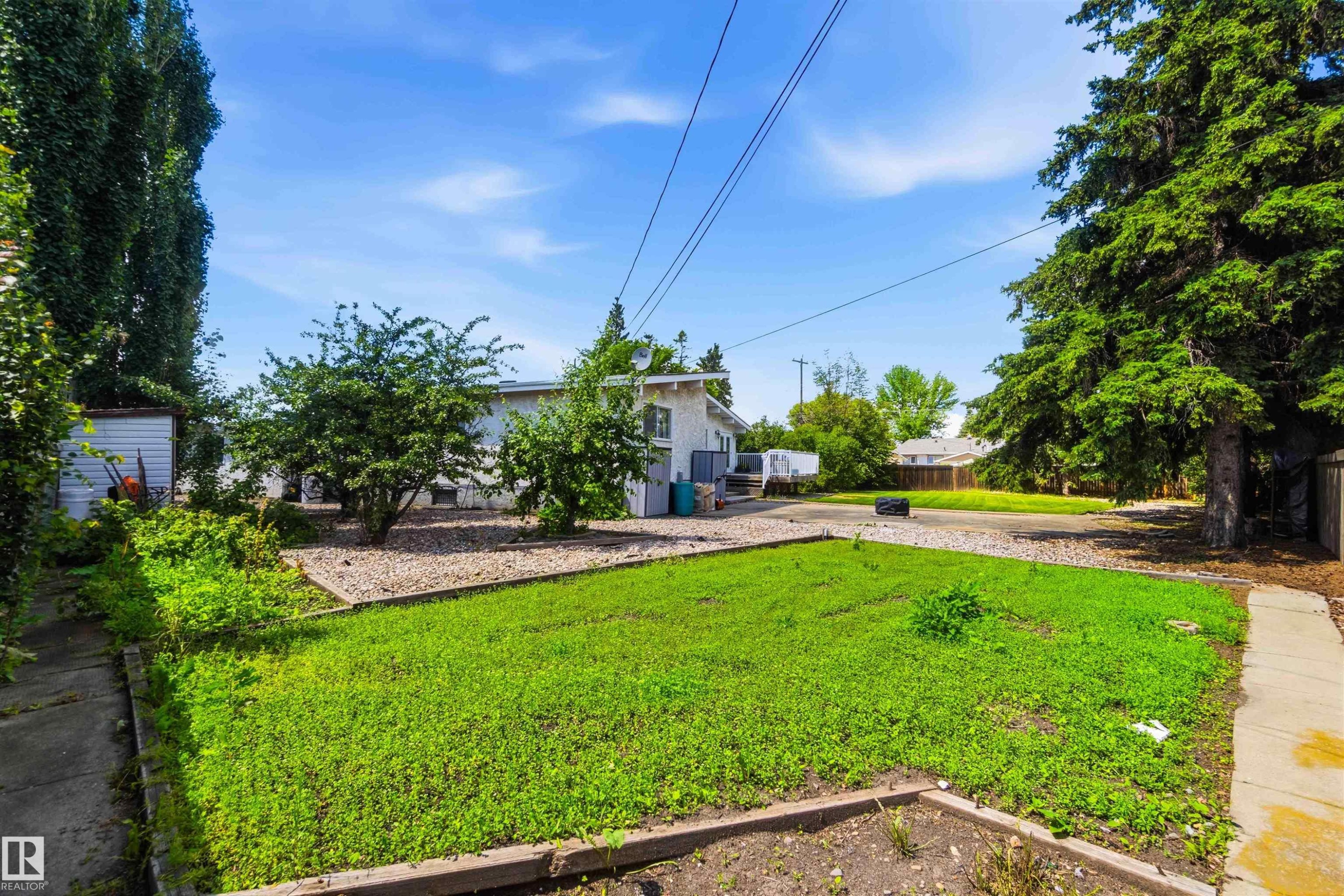 Expansive green space featuring a lawn area, mature trees, and landscaping elements with gravel and planted beds - 13121 122 Street, Edmonton, AB