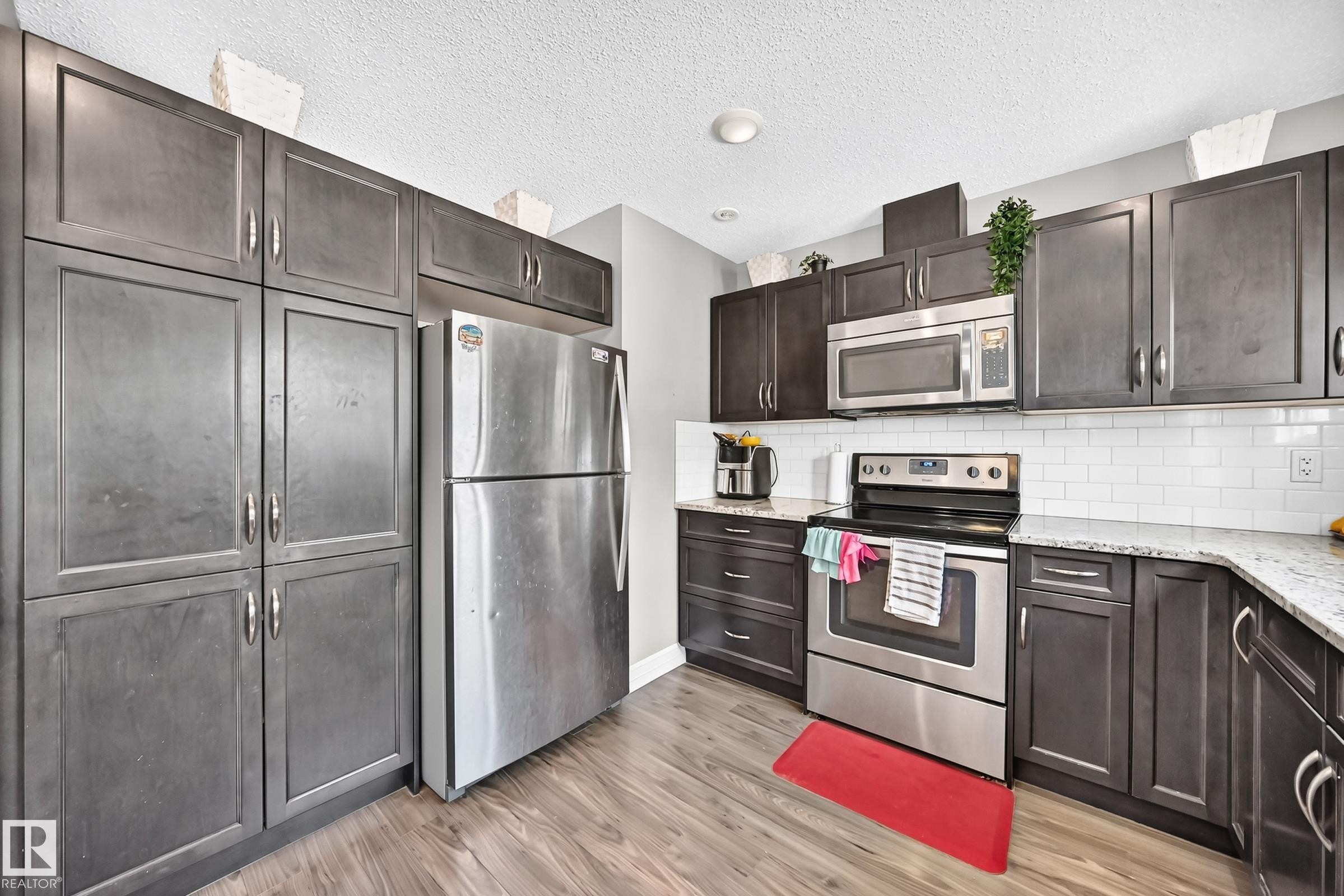 Kitchen featuring dark wood-finish cabinetry, stainless steel appliances, white subway tile backsplash, and light-toned countertops - 415 Clareview Rd Nw Nw, Edmonton, AB - Indoor Photo Showing Kitchen