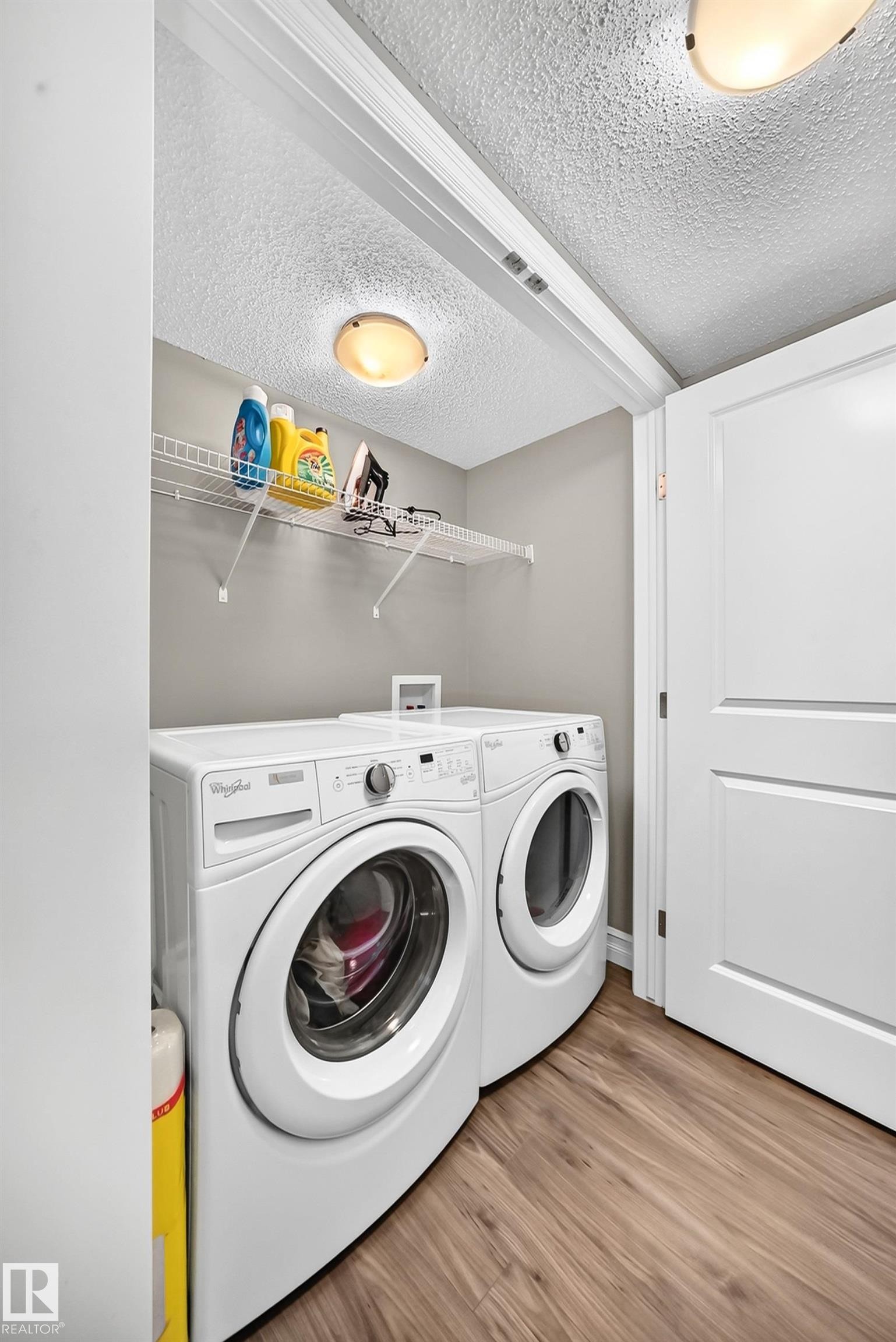 Dedicated laundry area featuring wood-finish flooring, light gray wall paint, and a white wire shelf - 415 Clareview Rd Nw Nw, Edmonton, AB - Indoor Photo Showing Laundry Room