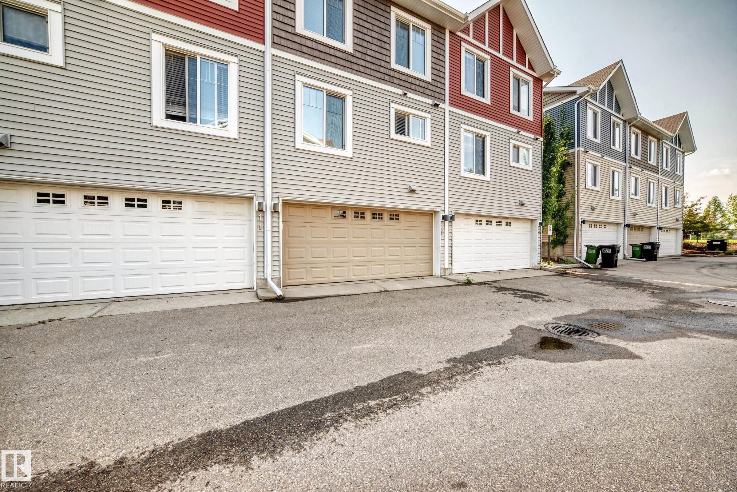Multi-level townhome exterior featuring horizontal siding, gabled rooflines, and individual garage access - 415 Clareview Rd Nw Nw, Edmonton, AB - Outdoor