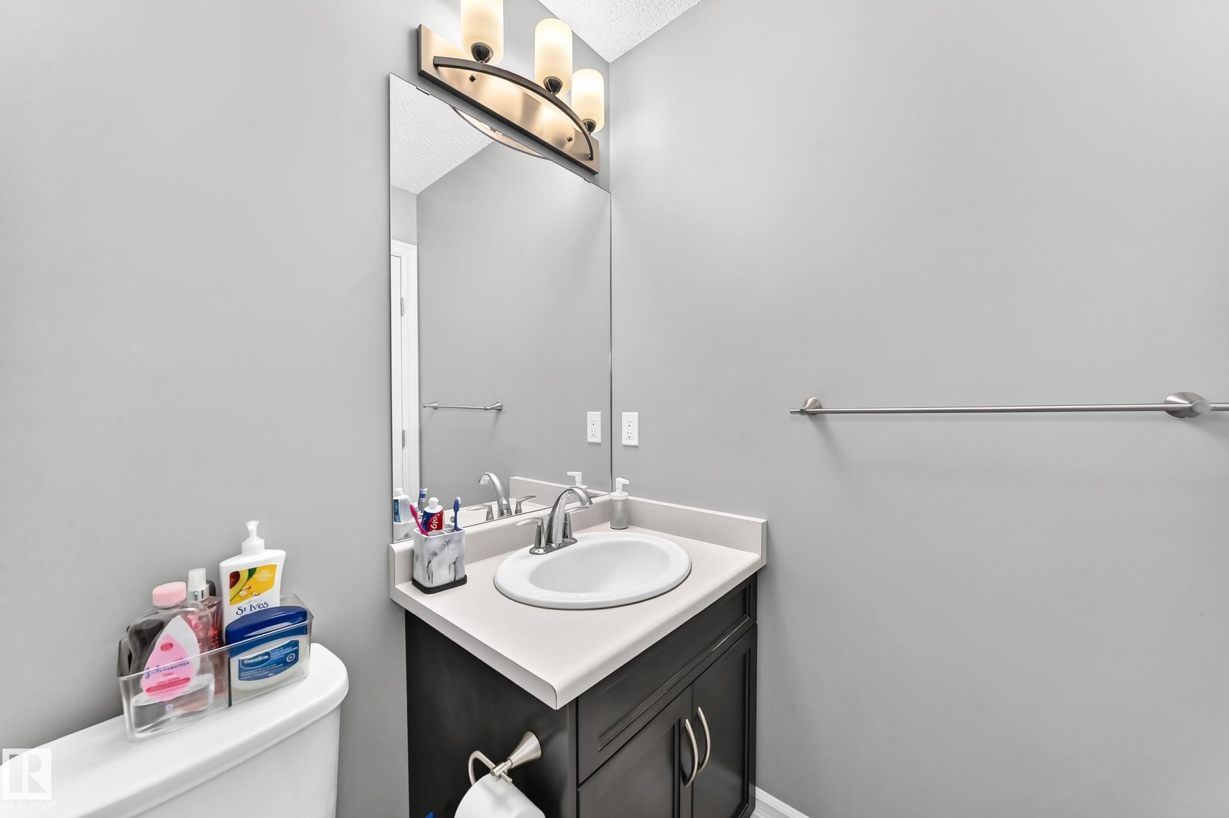 Compact bathroom featuring a single vanity with a white countertop and dark wood-finish cabinetry, under-mount sink, and chrome faucet - 415 Clareview Rd Nw Nw, Edmonton, AB - Indoor Photo Showing Bathroom