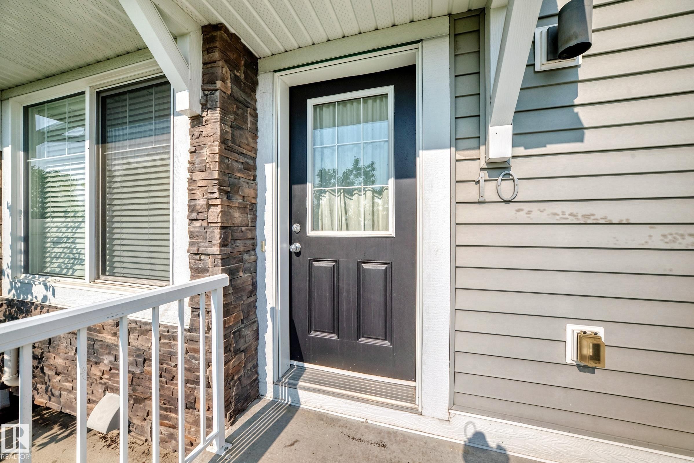 Entryway featuring a dark paneled door with an upper glass insert, complemented by a stone veneer column and light gray horizontal siding - 415 Clareview Rd Nw Nw, Edmonton, AB - Outdoor With Exterior